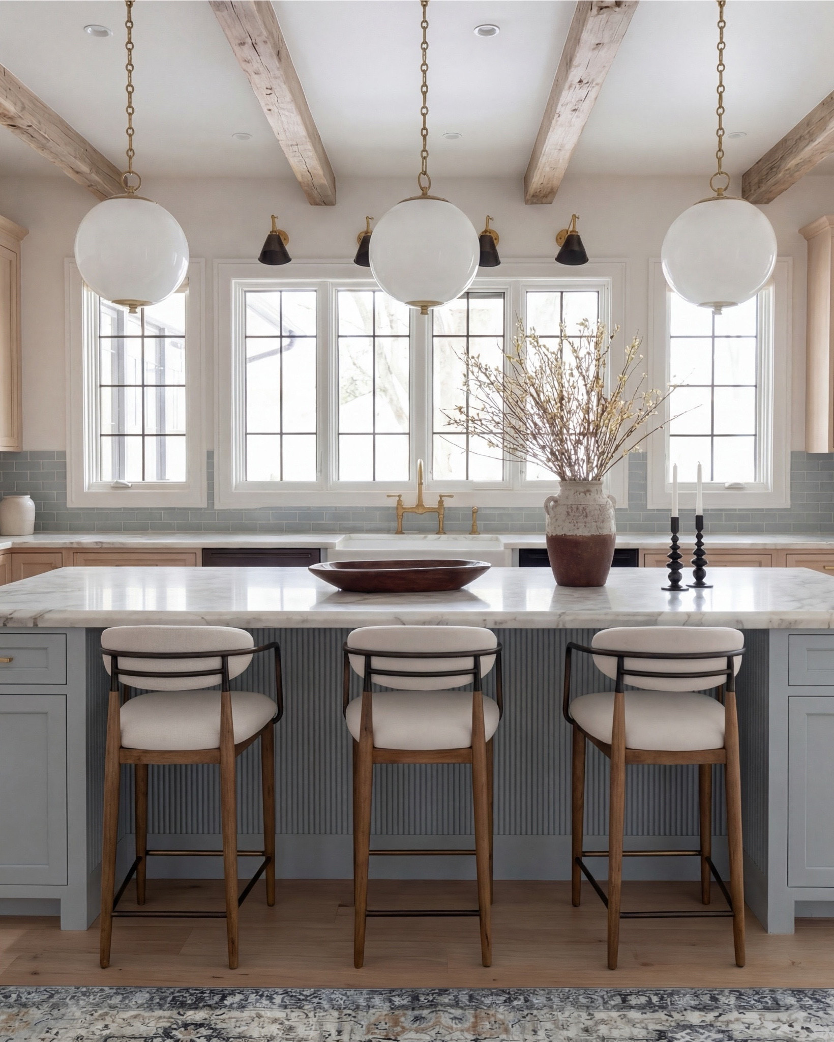 This kitchen is the definition of soft luxury done right. The pale blue island brings a calm, collected energy, while the warm oak cabinetry and exposed beams add that natural depth you can’t fake.

The oversized globe pendants keep everything feeling airy and modern, and the marble countertop? Effortless elegance. Even the runner pulls the whole palette together with those muted blues and warm neutrals.

It’s the kind of space that feels lived-in yet elevated—where morning coffee somehow tastes better and slow dinners feel intentional.

Shop the Look:
• Light blue fluted kitchen island
• Warm oak kitchen cabinets
• Brass globe pendant lights
• Marble kitchen countertop
• Neutral blue patterned runner
• Black + brass bar stools
• Soft blue subway tile backsplash
• Brown Ceramic vase with branches
• Gold kitchen faucet and hardware
• Brown bowl 
• Brown floral wall art
• Black candle holder

#LTKsale #LTKhome #LTKstyletip