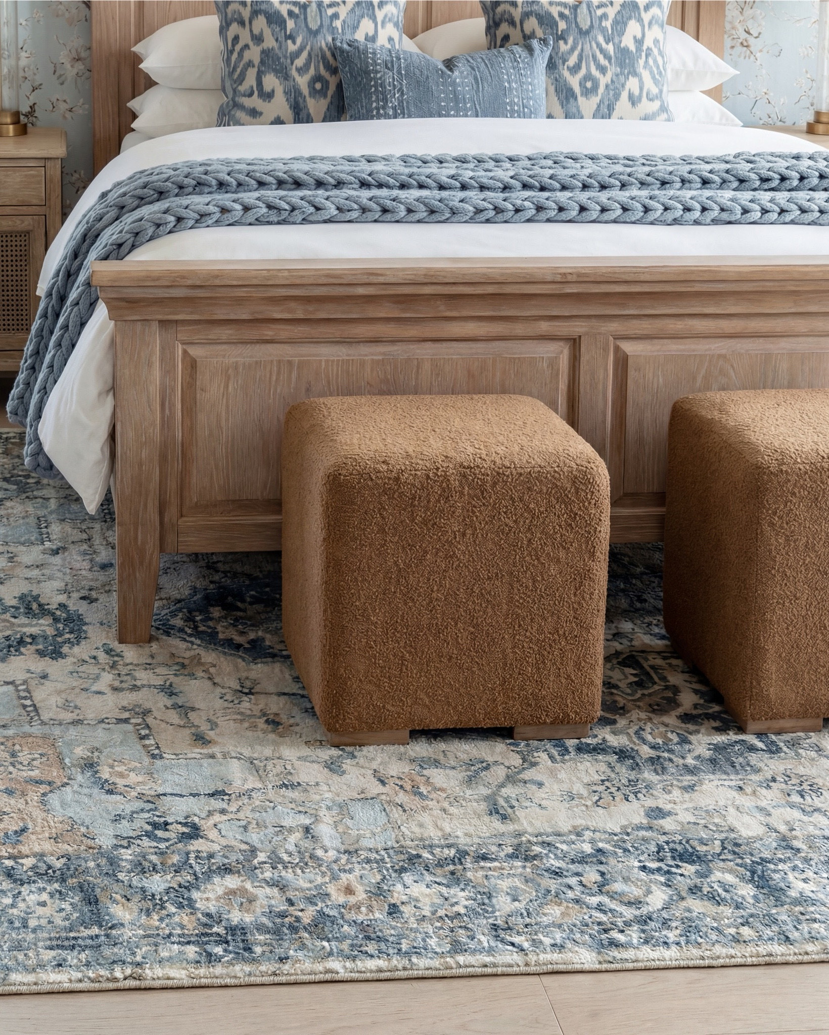 There is something so soothing about a bedroom that leans into soft blues, warm woods, and cozy layered textures — and this one is the perfect example of calm, elevated comfort.

The natural wood bed instantly warms the room, and I styled it with a chunky blue knit throw and patterned pillows to add that relaxed, lived-in layer of texture. The caramel cube ottomans at the foot of the bed bring in a rich contrast that grounds the palette beautifully.

The rug pulls everything together with its blend of soft blues and warm neutrals, adding just the right amount of pattern without overwhelming the space. The round brass beaded mirror is such a showstopper — it adds shine and dimension while playing so nicely with the brass details on the lamps.

And of course, the soft floral wallpaper and exposed beams make the entire room feel warm, airy, and collected. The perfect balance of cozy and polished.

✨ Shop the Look
Natural wood bed | Chunky blue knit throw | Patterned blue pillows | Caramel cube ottomans | Blue and neutral patterned rug | Brass beaded mirror | Brass table lamps | Soft floral wallpaper | Natural wood  cane nightstands | Exposed ceiling beams, ribbed white decor bowl.

#LTKsale #LTKstyletip #LTKhome