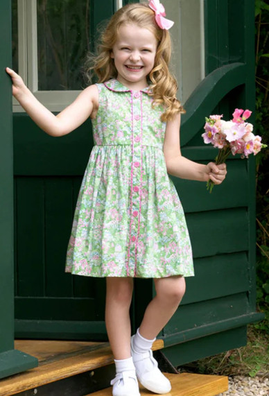 The Garden Floral Button-Front Dress captures the playful romance of a storybook summer. Rendered in a vibrant green ground with delicate pink florals and whimsical garden motifs, this beautifully tailored dress blends traditional British design with joyful childhood spirit. Crafted from premium breathable cotton, this sleeveless girls’ dress features a classic Peter Pan collar trimmed in contrast piping for a refined heritage finish. The full button-front closure, adorned with coordinating pink buttons and scalloped edging, adds both practicality and decorative charm. A softly gathered waist flows into a full skirt designed for twirling through garden parties, birthday celebrations, holidays, and family portraits. 

 #LTKmomlife #LTKKids #LTKWedding