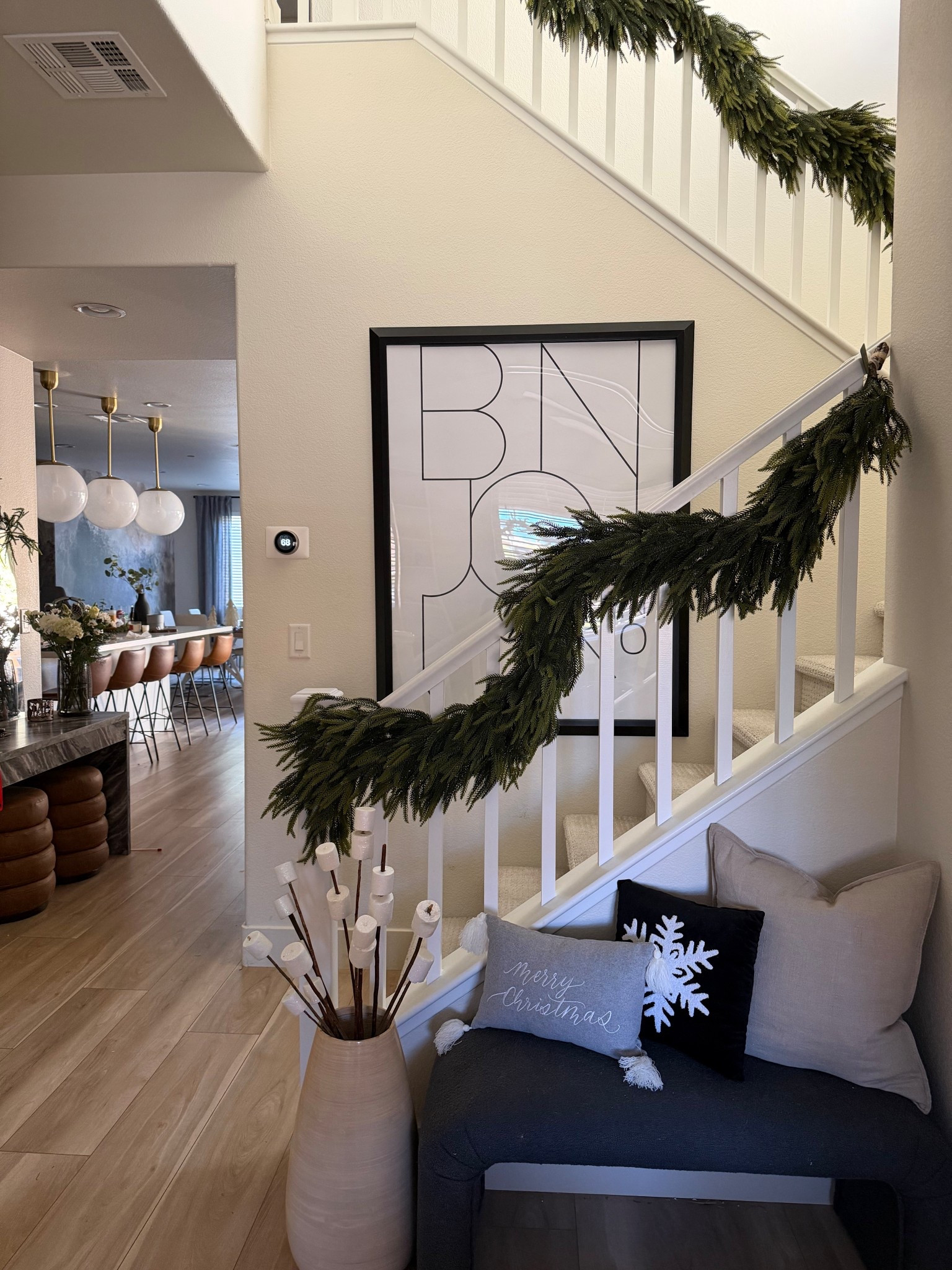 Neutral modern entryway with lush, realistic green garland draped along a white staircase. Three 6-foot strands used to create a full, designer-style holiday look. Minimalist decor with neutral bench, pillows, and tall floor vase.

#LTKSeasonal #LTKHoliday #LTKHome