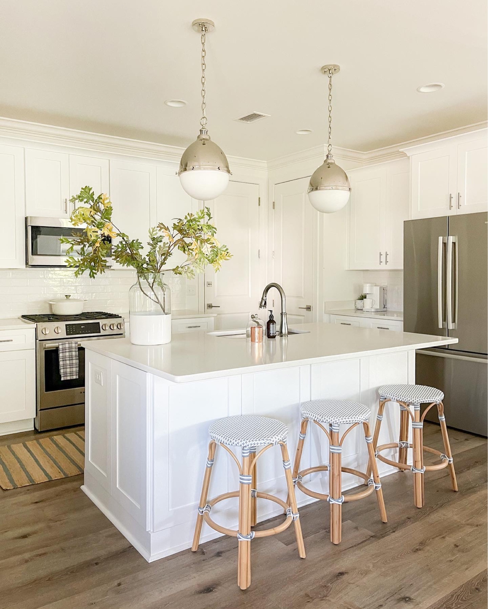 A view of our coastal cottage kitchen with designer look for less pendant lights, blue and white woven counter stools, and blue striped jute rug, paint dipped vase with faux oak leaves and the best scented hand soap!
.
#ltkhome #ltkseasonal #ltksalealert #ltkunder50 #tlkunder100 #ltkstyletip

#LTKhome #LTKsalealert #LTKSeasonal