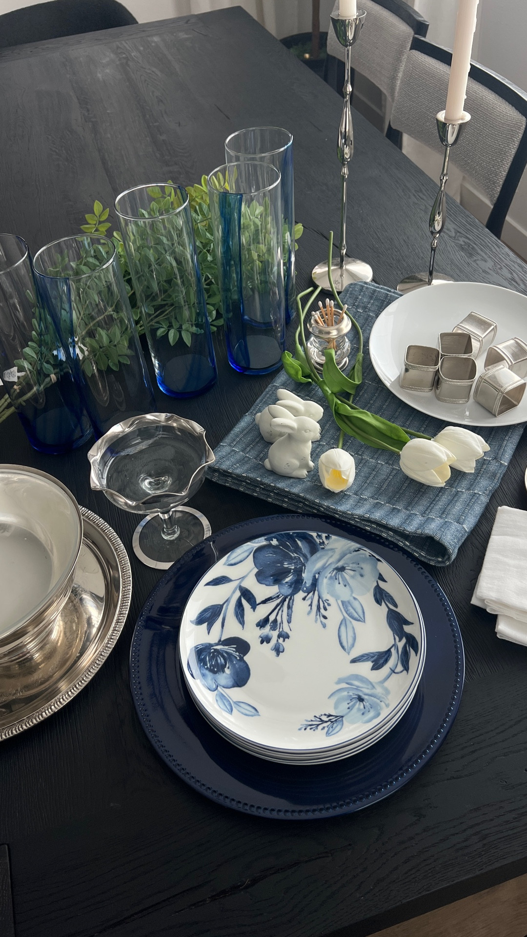 A modern blue and white Easter tablescape layered on a black wood table with tulips, silver accents, and classic place settings for an elevated yet effortless spring brunch. Blue and white table decor, Easter table decor, spring tablescape, black dining table, blue floral dinnerware, white plates, navy charger plates, linen napkins, napkin rings, tulip centerpiece, glass vases, silver candle holders, taper candles, bunny decor, neutral Easter decor, elegant table setting, hosting essentials, dining room decor, table styling, entertaining at home

#LTKHome #LTKSeasonal