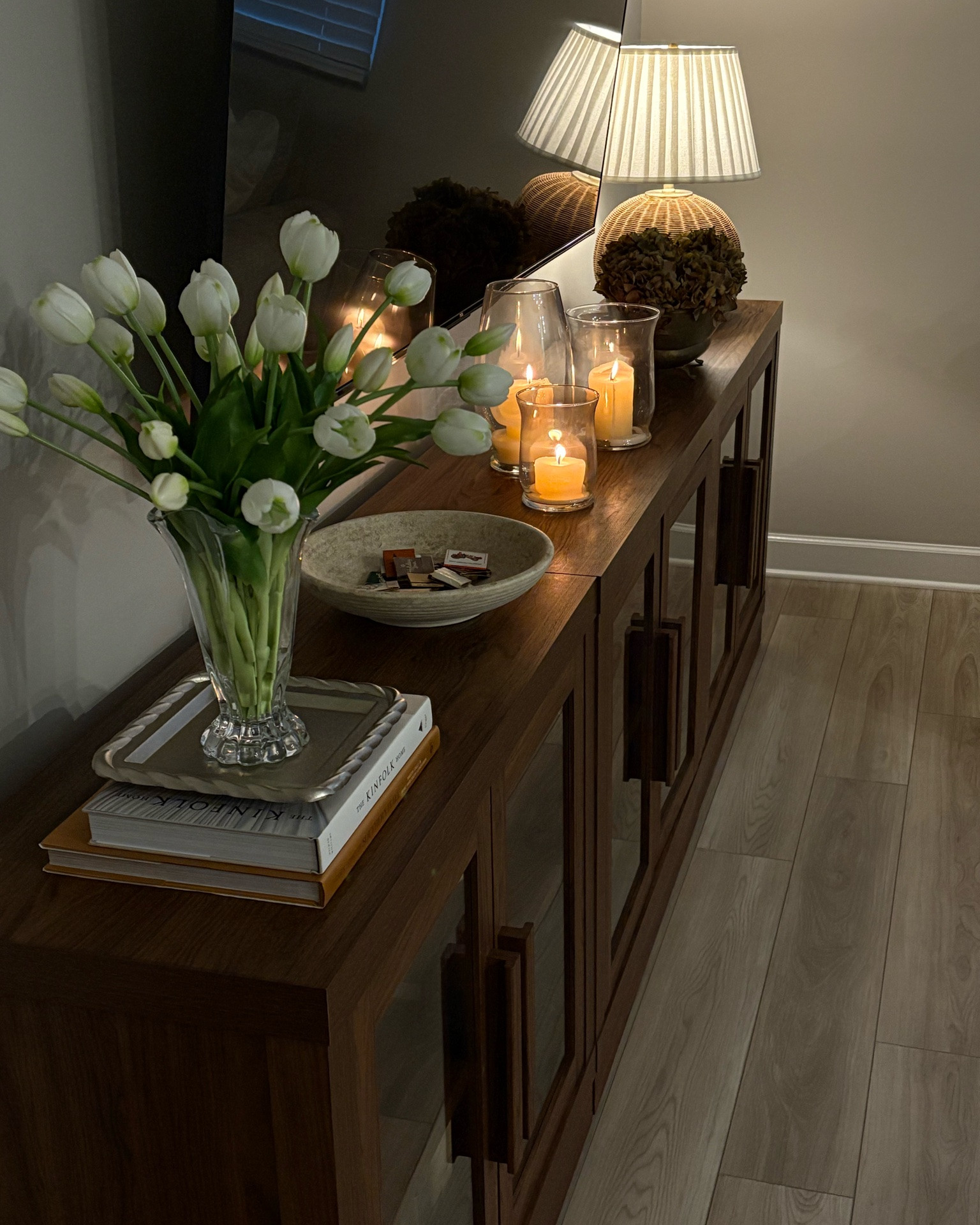 Mixing trending decor pieces with antiqued finds 🤎 A perfect balance to make a cozy home!! 

Tips for console table styling with a TV above: 
• Layer a few different groups of decor that won’t distract from TV - on our table I have a low profile bowl, gold antiqued footed bowl with hydrangeas, and hurricane vases with candles. None of which obstruct the TV! 
• On the outer corners where you can add more height, add a vase with florals and a lamp 
• Always mix textures and tones to make it interesting! I tend to choose wicker/rattan pieces, gold, silver, glass, metal, and wood. Added in some burlwood here too and love it! Then add in the florals for more texture. It all mixes together so well! 
• Ambient lighting whenever possible!!! Lamp and candles galore! Loving a hurricane vase with candle right now 🥰 
• Don’t overdo the decor on top - keep it classy and simple and not too distracting! 

Shelf styling: 
• Tips are similar, create groupings, utilize books, bowls, boxes, framed art, statement pieces, and vases to tie it all together
• When possible, have items on top of something and not “floating” - example are the books stacked with a tray, then a vase on top! Rather than just a vase, it elevates the space immensely!! 

#home #homedecor #consoletabledecor #interiordesign

#LTKHome