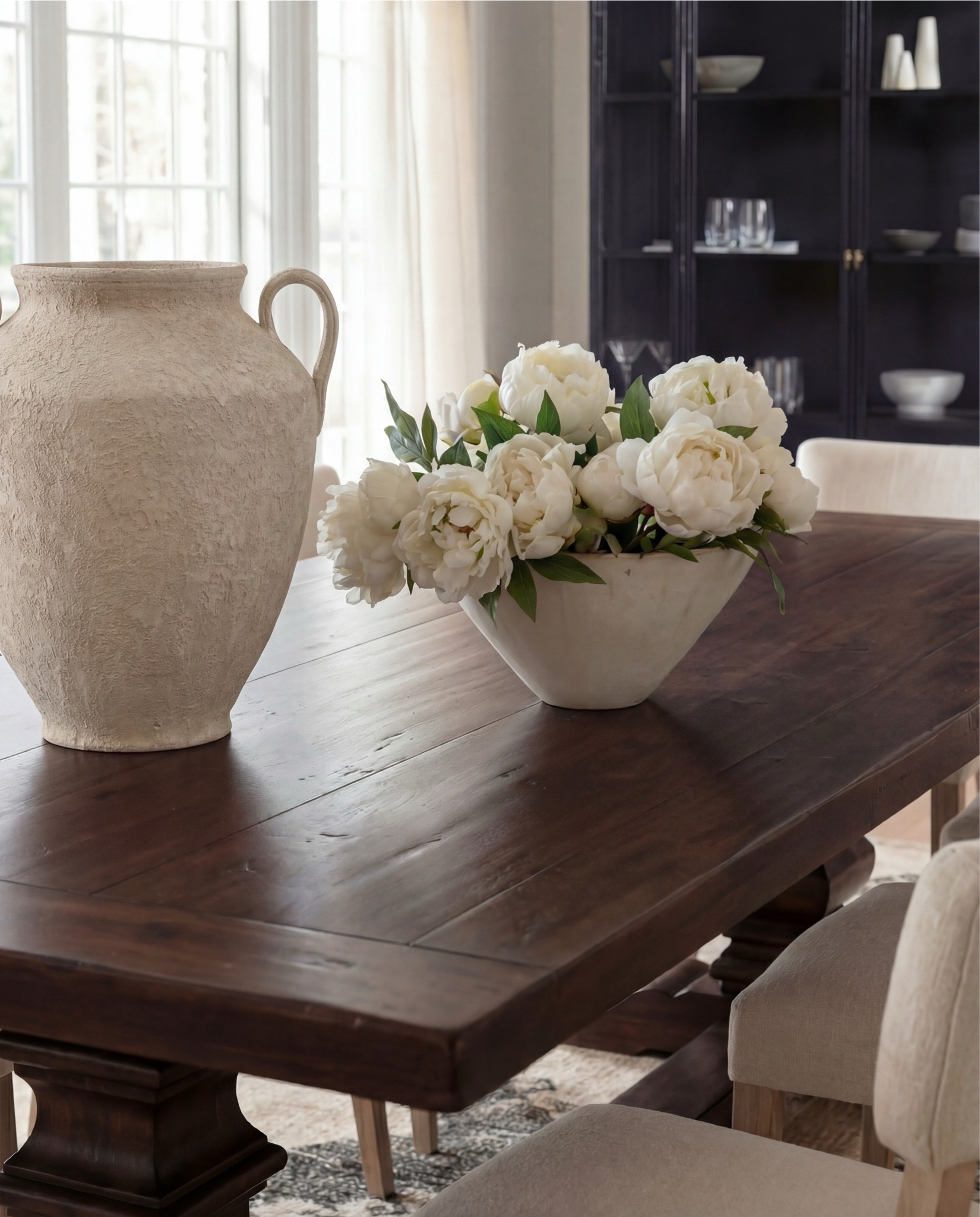 Shop the Look:
• Dark wood pedestal dining table
• Cream upholstered dining chairs with light wood legs
• Large neutral area rug with charcoal medallion pattern
• Black arched display cabinet / hutch
• Light wood sideboard / buffet cabinet
• Large ceramic floor vase (neutral tone)
• White ceramic bowl with white florals (peonies or roses)
• Pink faux cherry blossom stems in white vase
• Neutral ceramic table lamp with white shade
• Tall brass wall sconces with glass detailing
• Framed botanical artwork (set of four)
• Dark abstract wall art (large statement piece)
• White decorative vases (assorted sizes)
• Light linen curtains

#LTKSaleAlert #LTKHome