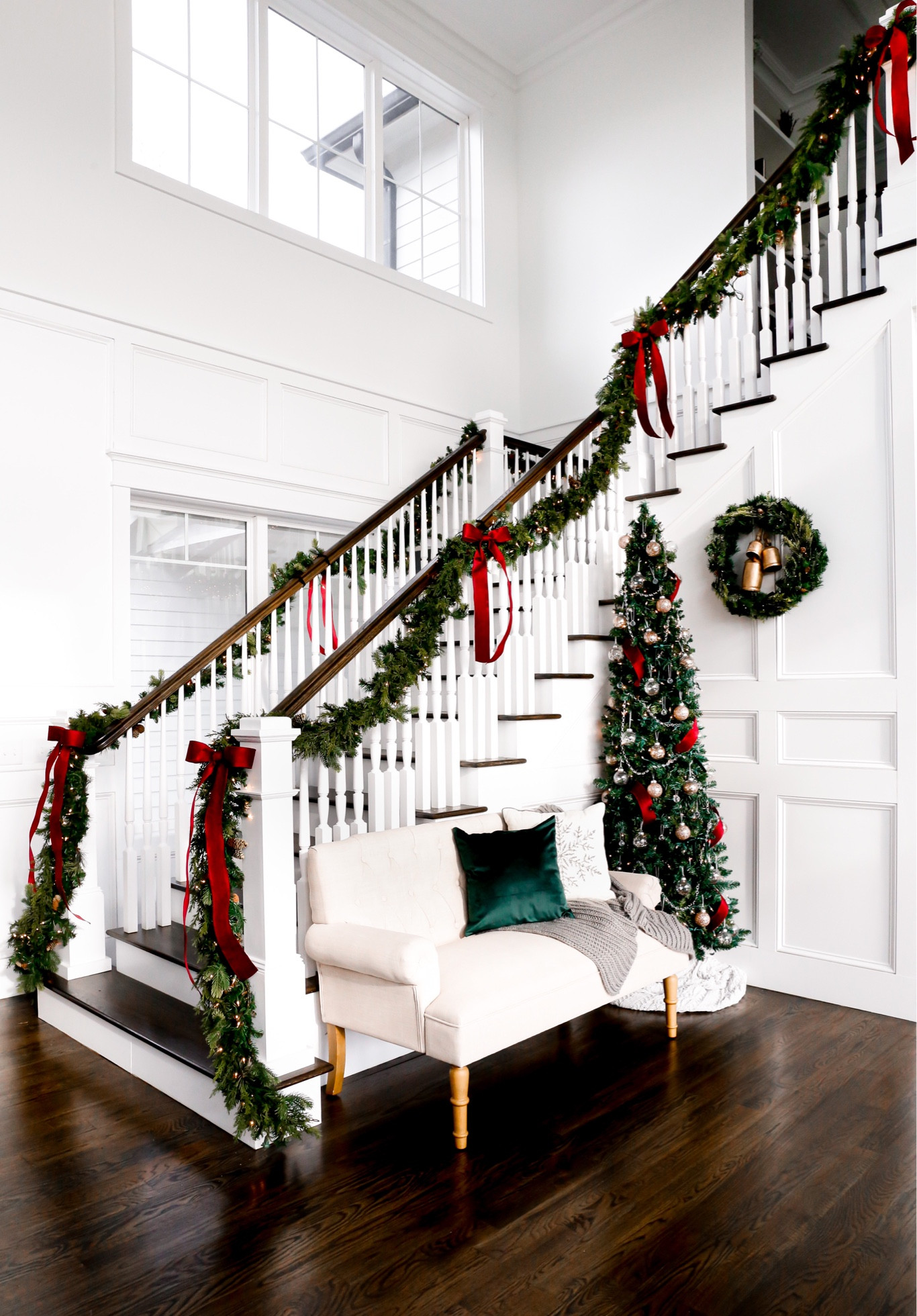Holiday themed staircase! With red oversized ribbons, layered garlands, pencil Christmas tree, wreath with gold bells, and more!

#LTKSeasonal #LTKHoliday #LTKhome