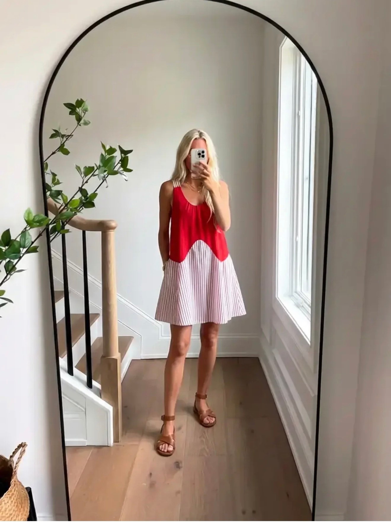 A bright lifestyle fashion mirror selfie in a modern home. A woman with long blonde hair stands in front of a tall arched black-framed mirror wearing a sleeveless red summer top paired with a light striped A-line skirt and brown leather flat sandals. The interior features light natural oak flooring, white walls, a staircase with a natural wood handrail and black metal balusters, and soft daylight streaming through a tall window. A leafy green branch adds an organic element to the space. The aesthetic is effortless summer fashion, coastal casual style, feminine warm-weather outfit, clean minimal interior, natural light lifestyle photography.

⸻

Caption

A little red moment for summer days. ❤️

⸻

Hashtags

#SummerStyle
#CasualChic
#ResortStyle
#EffortlessStyle
#VacationOutfit
#CoastalStyle
#FeminineStyle
#OOTDInspo
#SummerOutfitIdeas
#StyleInspoDaily
#ChicAndSimple
#MirrorSelfieStyle
#EverydayStyle
#CasualLuxury
#StyleInfluencer
#VacationStyle
#SummerWardrobe
#ResortWear
#TimelessStyle
#TravelStyle


#LTKSpringSale #LTKdayinmylife #LTKgrwm