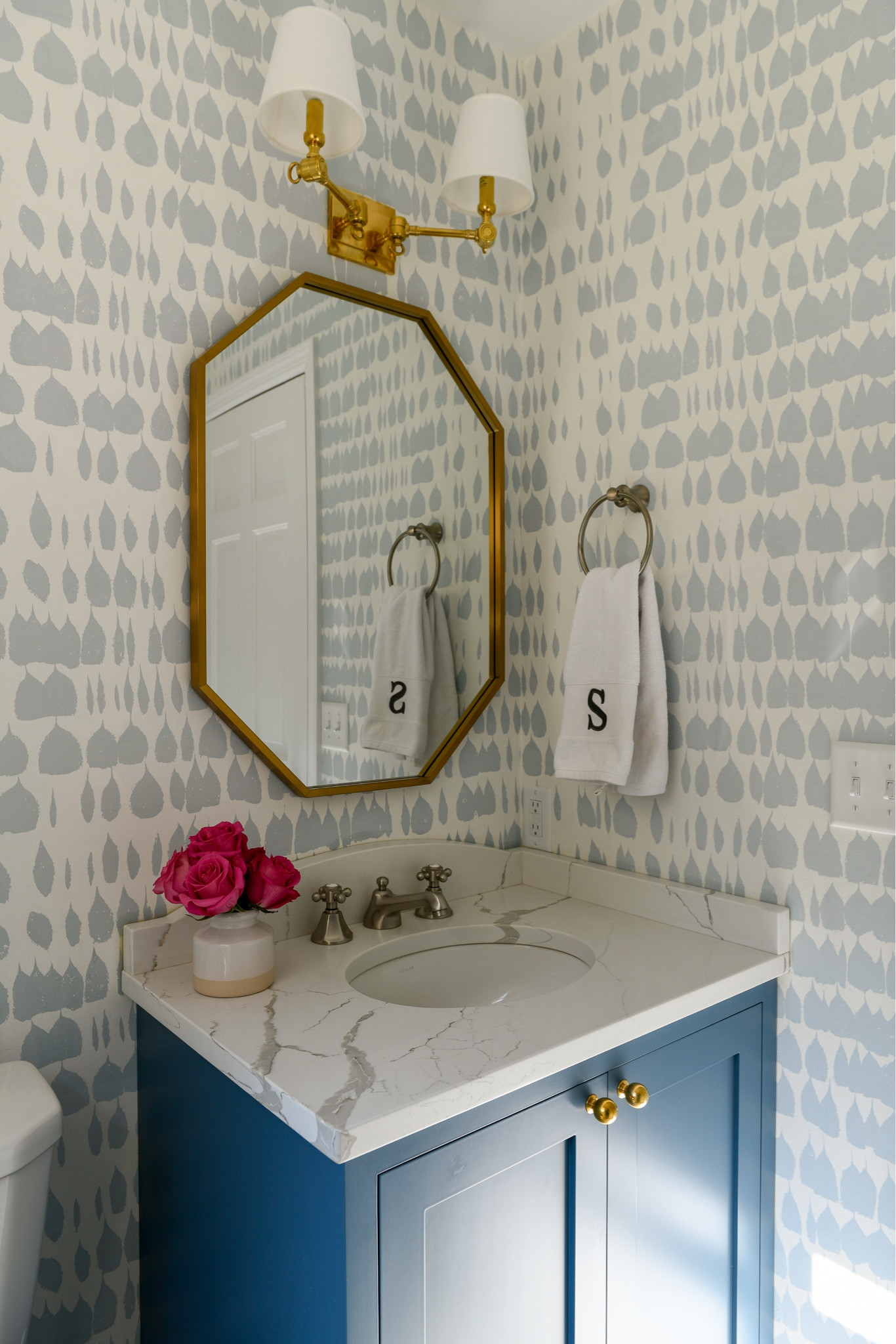 A classic powder room design with a brass sconce, brass mirror, nickel faucet, Schumacher Queen of Spain wallpaper, calacatta gold marble hexagon tile and custom blue vanity with brass gold knobs. 

#LTKhome #LTKFind #LTKstyletip