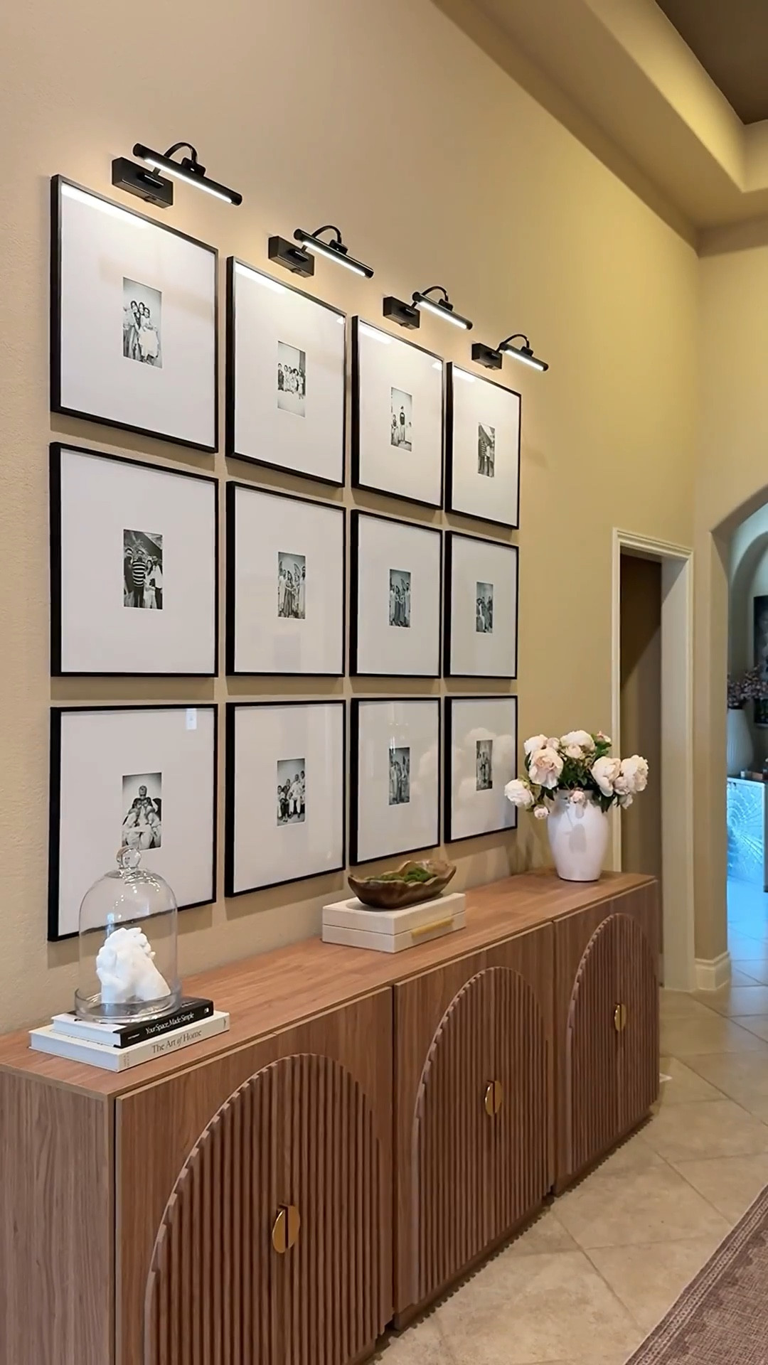 Created a gallery wall with 12 of our favorite family photos framed in clean black frames. To ground the space, I styled 3 fluted cabinets side by side to give the look of a long credenza. Added battery-operated picture lights, peonies in a white vase, and a few coffee table books for layered, timeless styling. @wayfair @walmart @amazon 

#LTKStyleTip #LTKHome #LTKSaleAlert