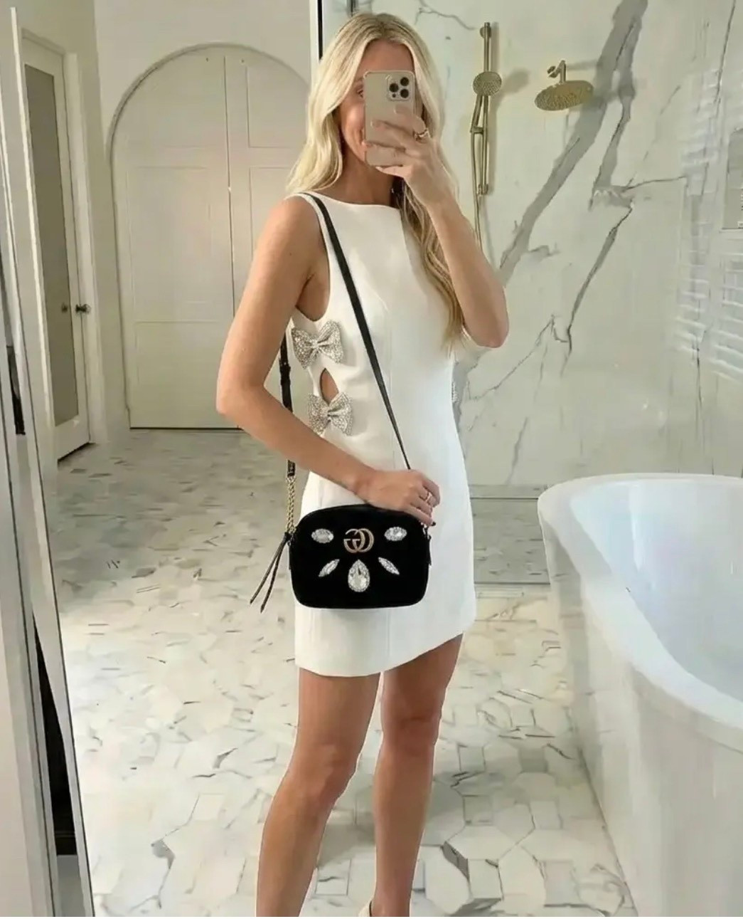 A chic mirror selfie in a bright, marble luxury bathroom with soft natural lighting. A tall, elegant blonde woman wears a structured white mini dress featuring delicate side cutouts adorned with crystal bow details. She styles the look with a black embellished crossbody bag and minimal black heels. Her hair is worn in loose, polished waves, and the overall mood feels modern, feminine, and refined — blending quiet luxury, Parisian-inspired elegance, and subtle statement details.

⸻

HASHTAGS

#QuietLuxury
#WhiteDressMoment
#BowDetails
#ModernElegance
#FeminineChic
#LuxuryAesthetic
#ParisianStyle
#MinimalistFashion
#SoftGlam
#ClassicWithATwist
#ChicOutfit
#MirrorStyle
#TimelessFashion
#StatementDetails
#OOTD
#OldMoneyVibes
#ElegantLook
#NeutralLuxury
#MainCharacterEnergy
#EffortlessChic

#LTKdayinmylife #LTKGiftGuide #LTKHoliday