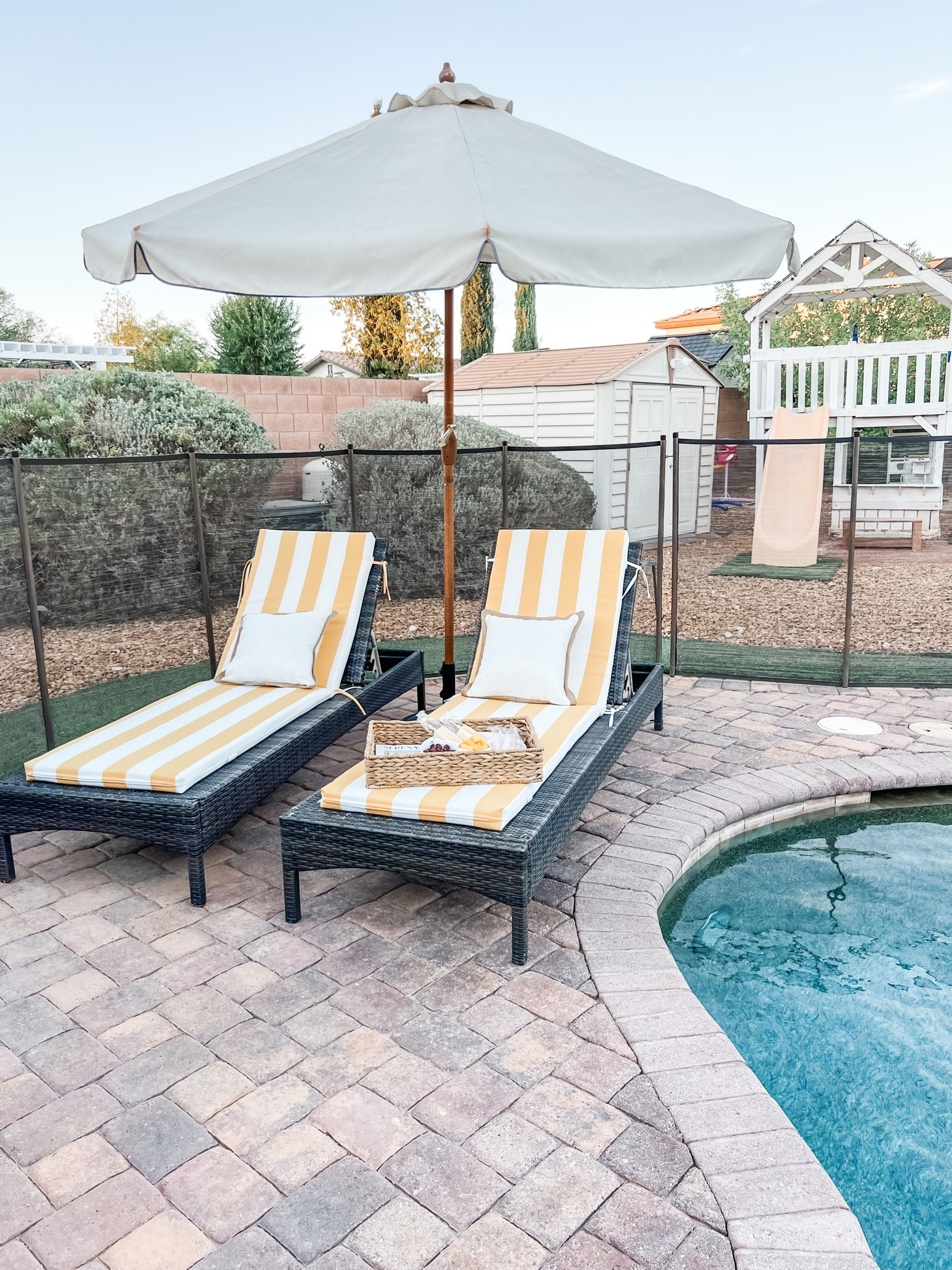 Loving this pool set-up!  
🍋 Wicker lounging chairs with yellow cabana striped cushions.  Painted playhouse, faux wood umbrella with scalloped edge, woven serving tray, & white outdoor pillows.

#LTKhome #LTKSeasonal #LTKfamily