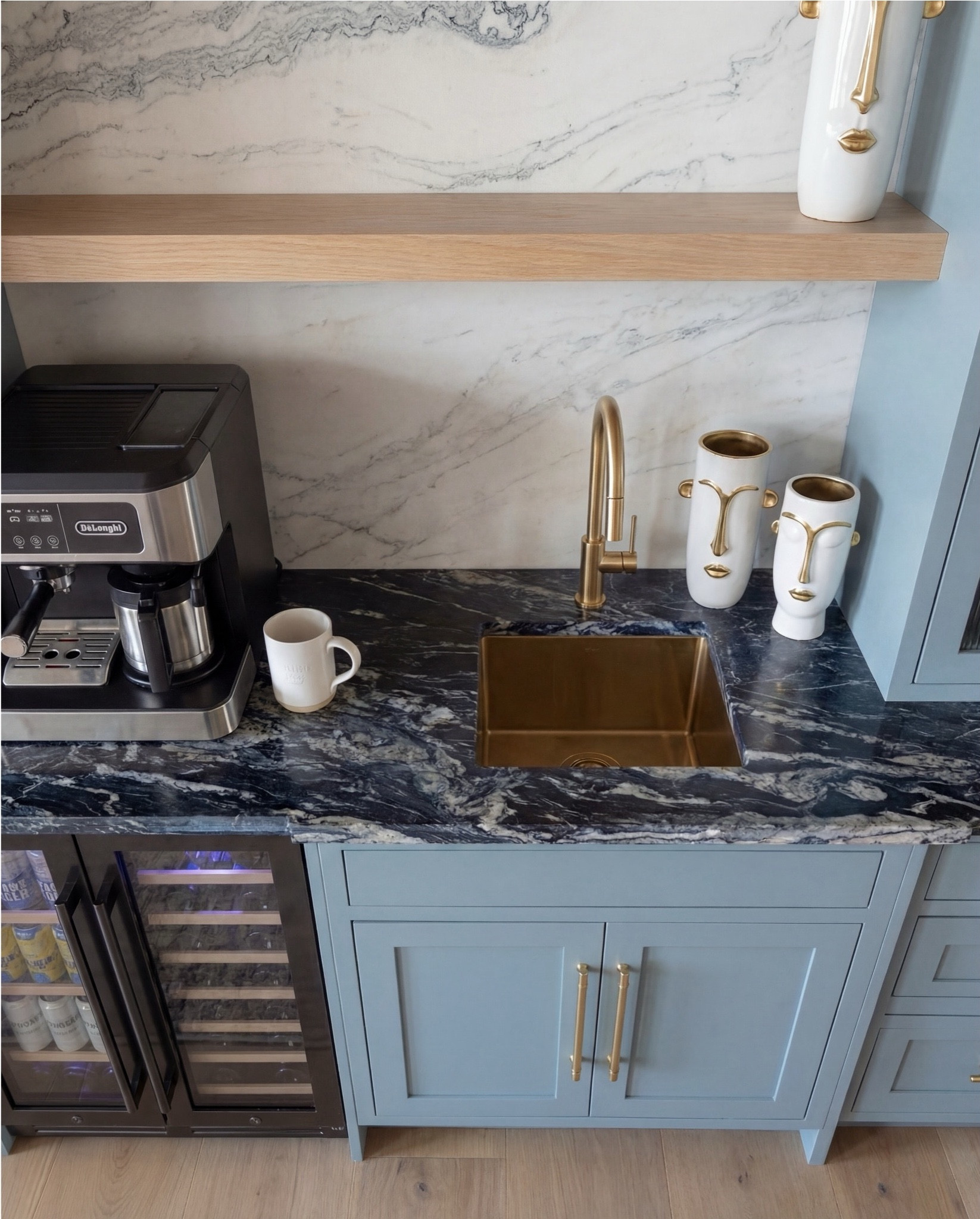 Shop the Look:
• Soft blue paneled cabinetry
• Brass cabinet pulls + drawer handles
• Fluted glass upper cabinet doors
• Marble slab backsplash (gray veining)
• Dark marble countertops
• Brass wall sconces with white shades
• Built-in beverage fridge
• Built-in wine fridge
• Stainless steel coffee maker
• Brass gooseneck bar faucet
• Undermount bar sink
• Light wood floating shelf
• Decorative ceramic face vase (white + brass details)
• Wood ceiling with dark exposed beams
• Vintage-style runner rug (neutral pattern)
• Light wood flooring



#LTKSaleAlert #LTKHome