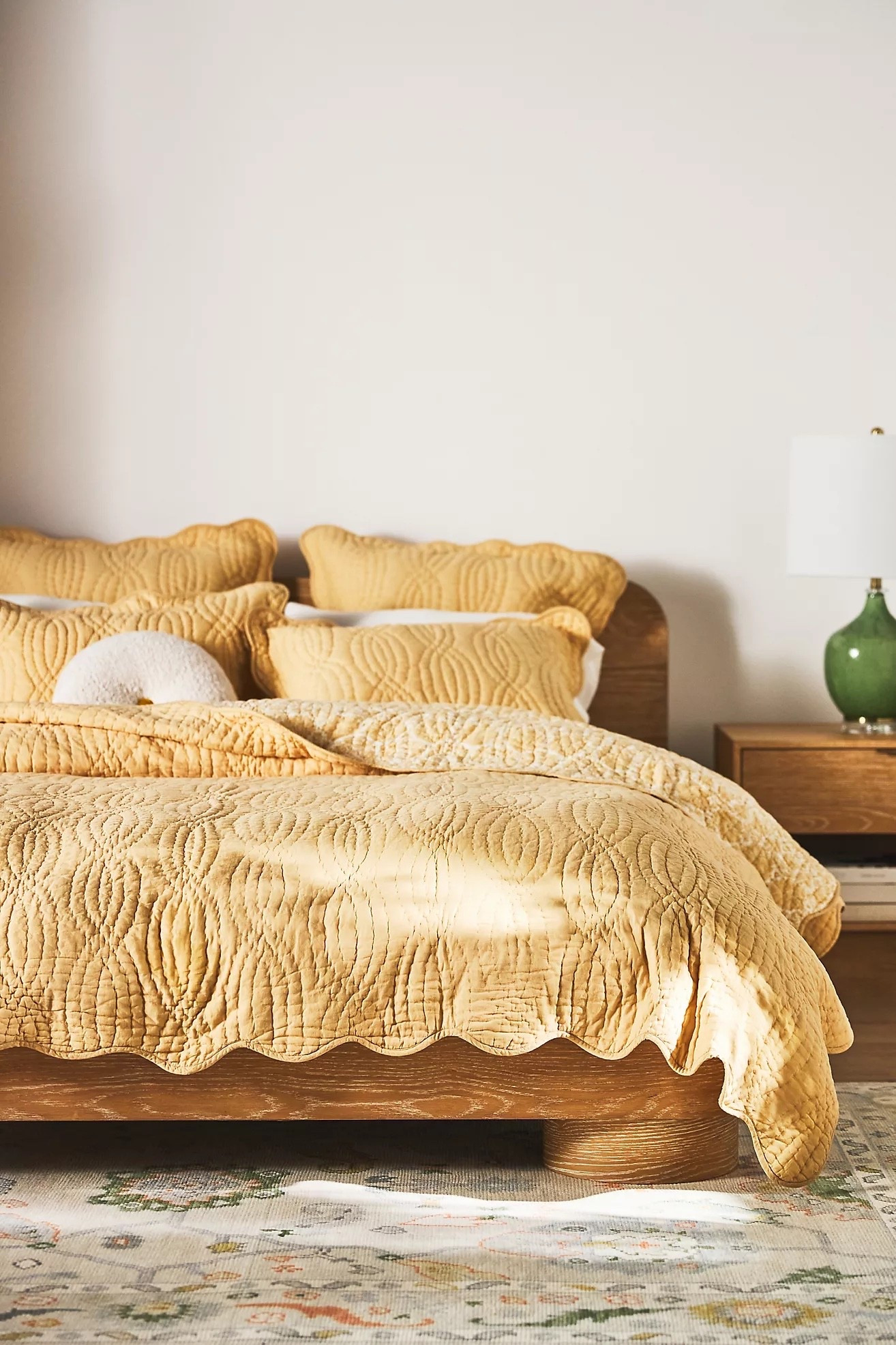Guest bedroom has sunny yellow sheets and a rich ochre linen duvet. 2 sunny sheet pillows, 2 brown linen sham pillows, and 2 extra yellow quilted throw pillows create an enveloping bed. Add a wavy checkered throw blanket and a green rug for an inviting an fun guest room. 

