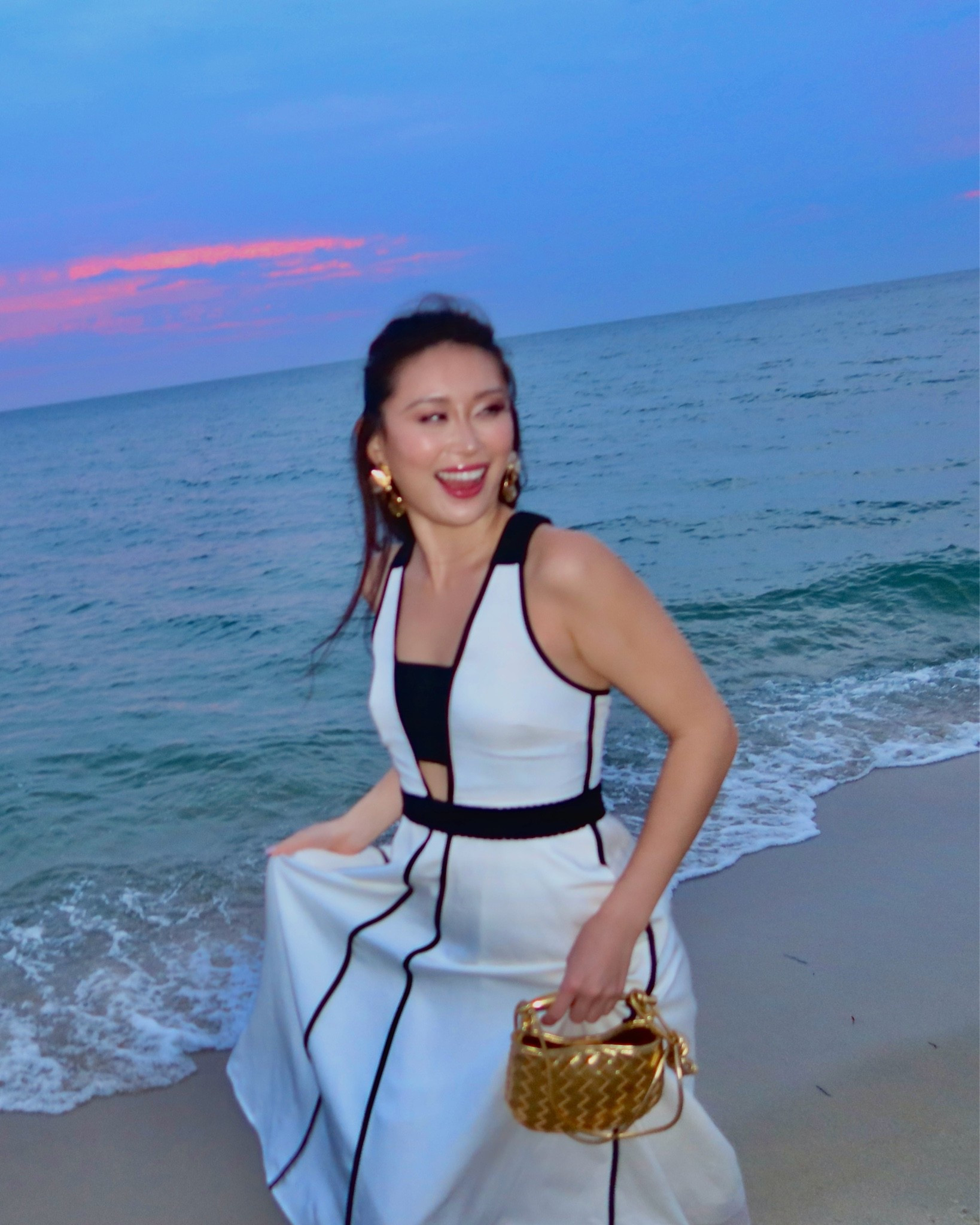 the reiss white linen maxi dress in size 4 — a structured sleeveless maxi with black contrast piping along the seams, a deep v-neckline with center cutout, and a fitted bodice with full skirt — styled with a gold woven mini bag and gold statement earrings for a barefoot twilight walk on the beach. the crisp white linen and graphic black piping make this the perfect quiet luxury statement dress for elevated coastal evenings. perfect for nantucket evenings, hamptons beach dinners, newport twilight strolls, and east coast summer getaways. shop this look linked above.