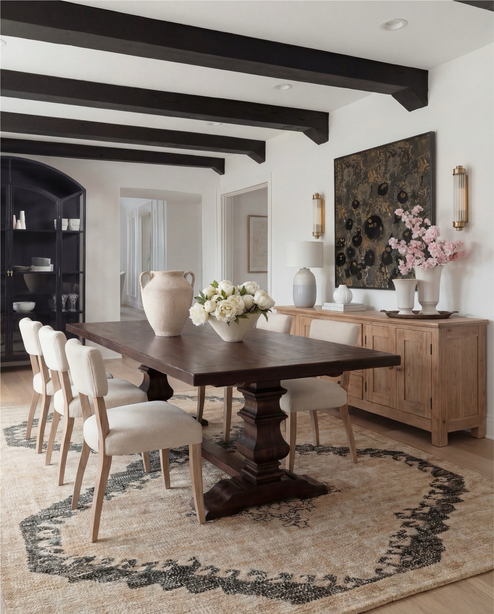 Shop the Look:
• Dark wood pedestal dining table
• Cream upholstered dining chairs with light wood legs
• Large neutral area rug with charcoal medallion pattern
• Black arched display cabinet / hutch
• Light wood sideboard / buffet cabinet
• Large ceramic floor vase (neutral tone)
• White ceramic bowl with white florals (peonies or roses)
• Pink faux cherry blossom stems in white vase
• Neutral ceramic table lamp with white shade
• Tall brass wall sconces with glass detailing
• Framed botanical artwork (set of four)
• Dark abstract wall art (large statement piece)
• White decorative vases (assorted sizes)
• Light linen curtains

#LTKSaleAlert #LTKHome
