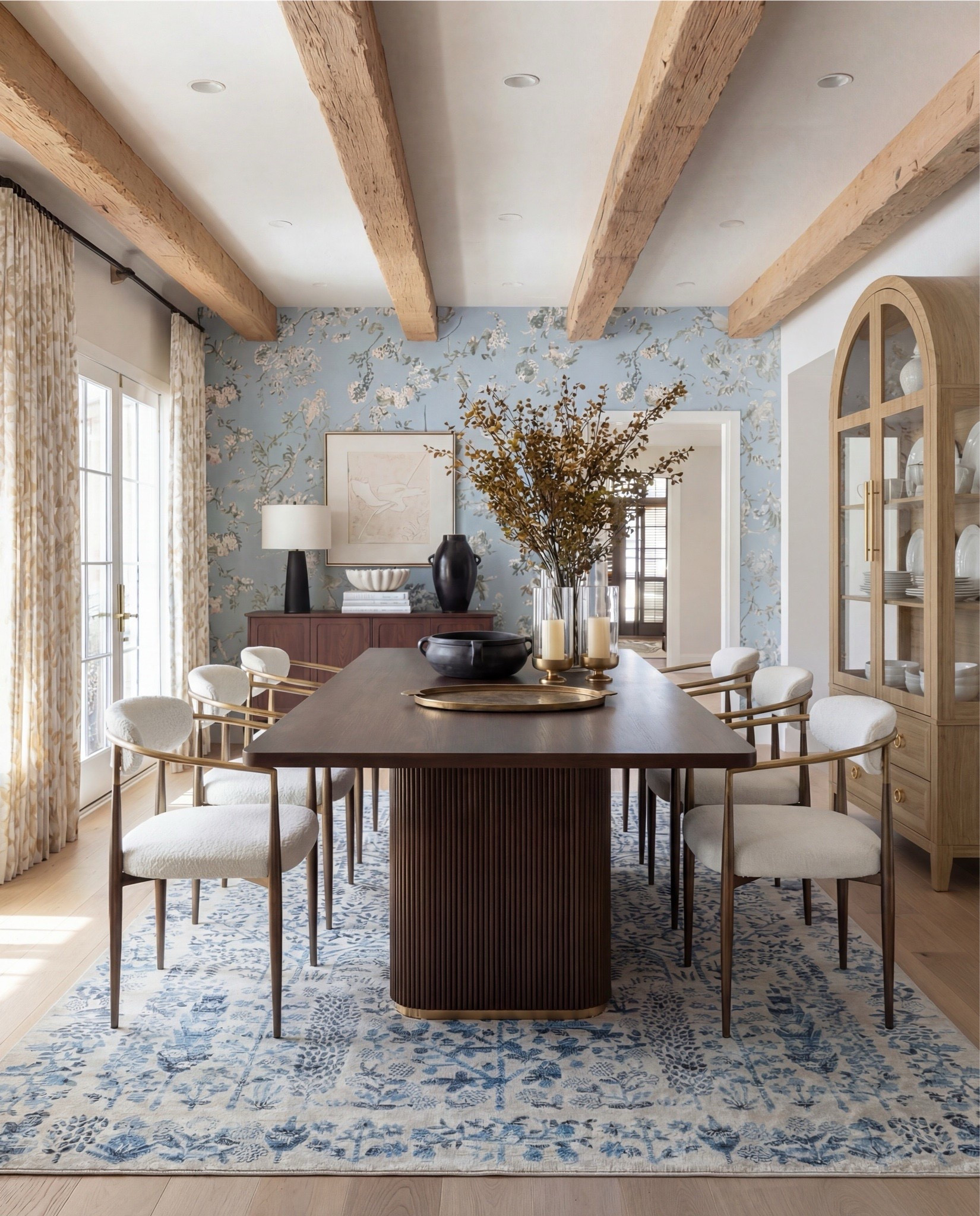This dining room feels like a pause in time—in the best way. The soft blue floral wallpaper instantly sets the mood, while the exposed wood beams ground the space and keep it from feeling too formal. It’s classic, but approachable.

What really makes this room work is the balance: the sculptural wood dining table anchors everything, while the light, upholstered chairs keep it airy and inviting. Brass accents add just enough warmth, and that blue patterned rug quietly ties the walls to the floor without competing for attention.

It’s elegant, intentional, and designed for long dinners that turn into even longer conversations.

Shop the Look:
• Solid wood dining table
• Upholstered dining chairs with brass frames
• Blue floral wallpaper
• Blue patterned traditional rug
• Wood ceiling beams
• Glass candle holders
• Black ceramic bowl decor
Black ceramic vase
Brass serving tray
Solid wood buffet console
Solid oak tall cabinet
Black ceramic decor bowl
White decor books
Black table lamp, white fluted decor bowl
• Neutral linen curtains
• Wood display cabinet with glass doors

#LTKHome #LTKSpringSale #LTKSaleAlert