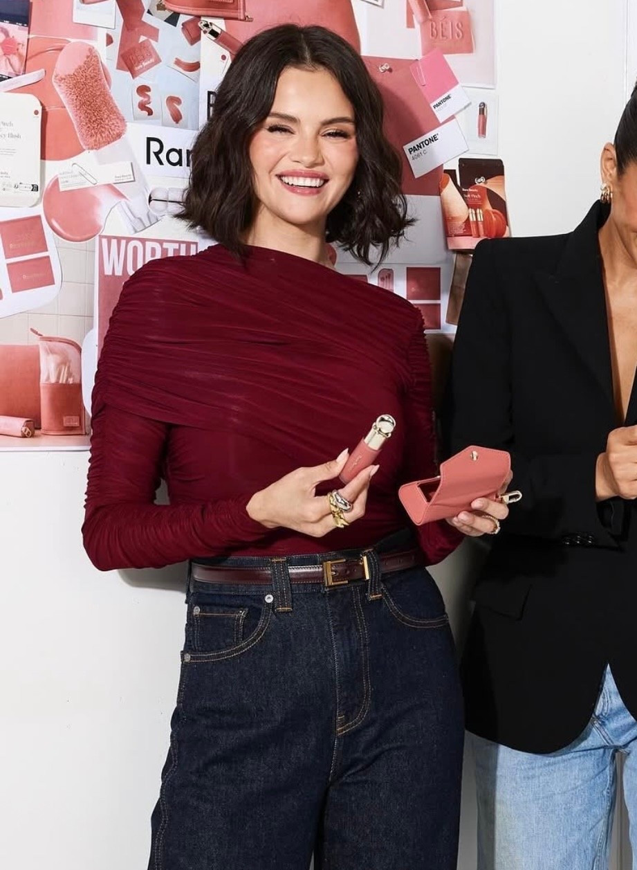 Selena Gomez draped long sleeve bodysuit dark rinse jeans leather belt liquid blush and travel case