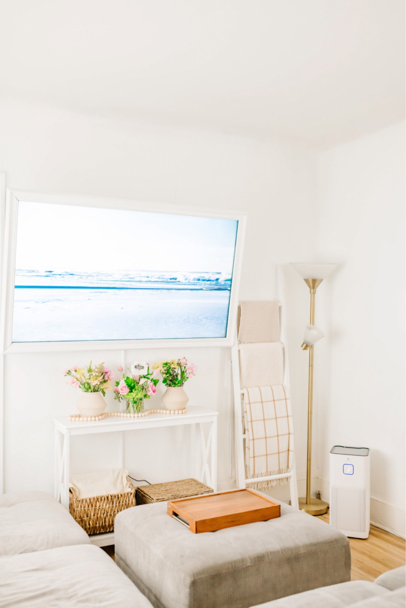 Warm and minimal living room with neutral colors gray couch, beach scene on TV white ladder with cozy, blankets, white entryway table under the TV, air purifier, lighting, clean 

#LTKFind #LTKhome #LTKunder100