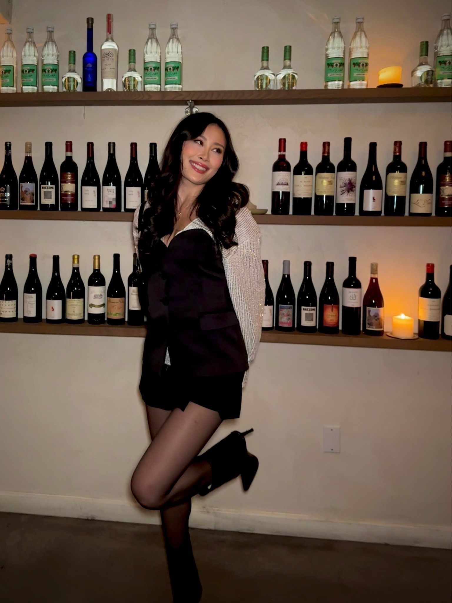 a black corset bodice mini dress with statement silver sequin long sleeves, styled with sheer black tights and black pointed-toe heels for a candlelit night at a natural wine bar in nyc. the contrast of the structured black bustier with the sparkly sleeves makes this the perfect festive going-out outfit. perfect for nyc wine bars, holiday cocktail parties, candlelit date nights, and downtown winter dinners. shop this look linked above.
