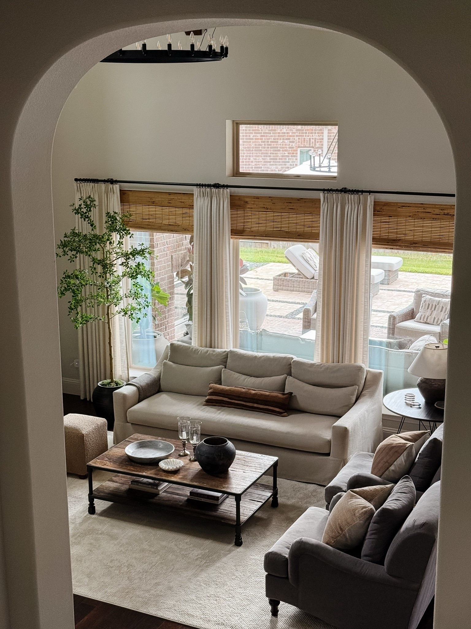 Neutral living room furniture, custom linen drapes with bamboo shades, cream slipcovered sofa, gray armchairs, and faux black olive tree