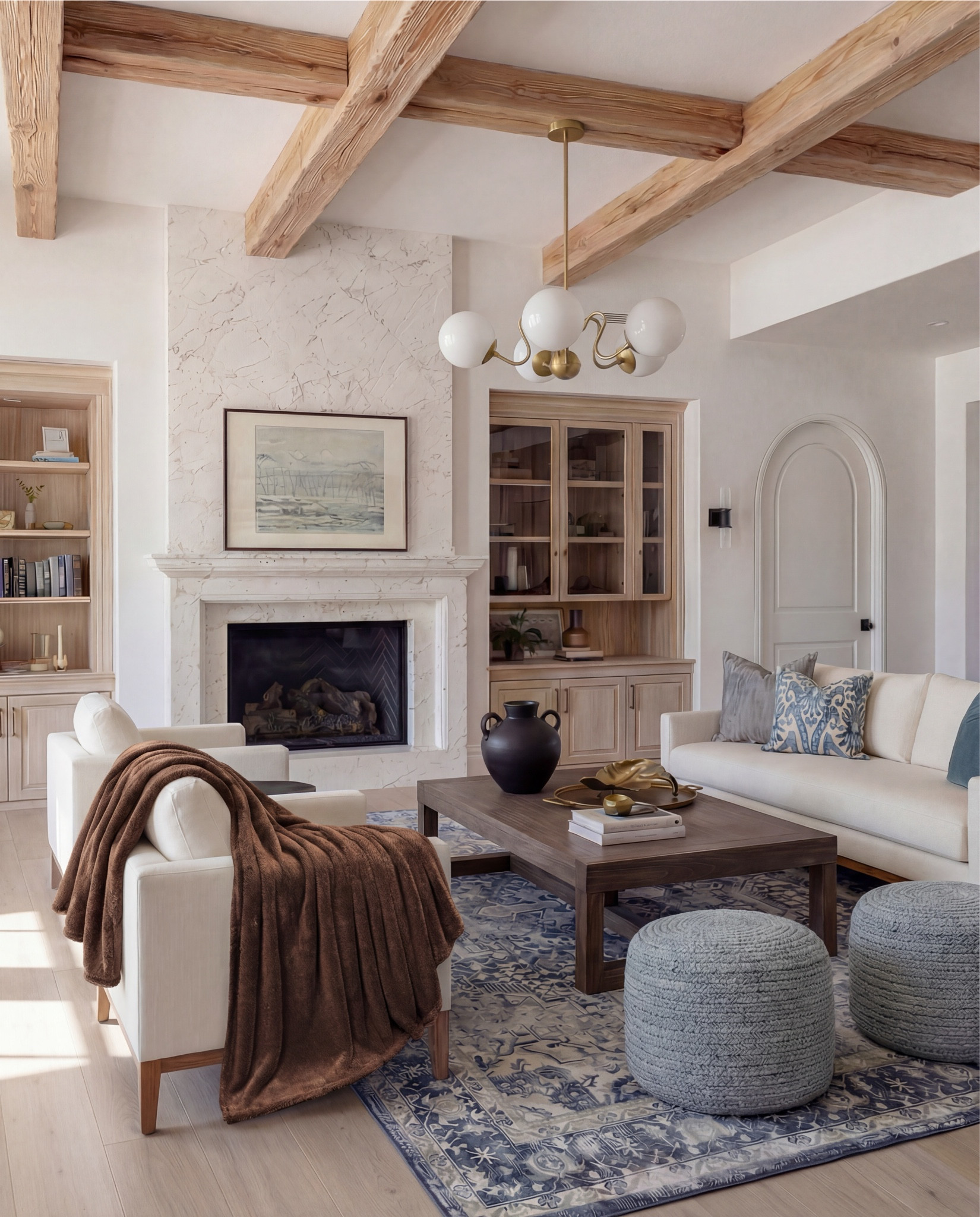 This living room is the definition of quiet luxury meets warmth. The moment you walk in, your eye goes straight to that marble fireplace—soft veining, classic silhouette, and framed by built-ins that add so much character without trying too hard.

The palette is what makes it magic: creamy upholstery, layered blues, and those chunky knit ottomans that bring in the perfect hit of texture. I love how the wood beams echo the cabinetry and pull the whole space together—it feels curated, intentional, and lived-in all at once.

It’s elegant but still cozy…the kind of room that invites you to sit down and stay awhile.

Shop the Look:
• Marble fireplace surround
• Cream armchairs + sofa
• Blue patterned lumbar + throw pillows
• Chunky knit ottomans
• Solid wood coffee table
• Black ceramic vase decor
• Distressed blue traditional rug
• Wood built-ins with glass fronts
• Warm wood ceiling beams
Brown throw blanket 
White decor books
Brass oval tray
Black decor bowl
Rounded globe chandelier 

#LTKFindsUnder100 #LTKSaleAlert #LTKHome