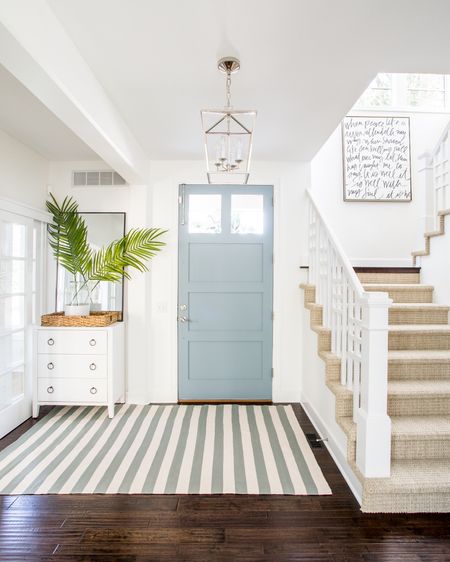 Our Omaha entryway decorated for summer with a white glossy raffia cabinet, blue and cream striped rug, lantern pendant light, “It Is Well” canvas art, tall thin black framed mirror, faux palm leaves and a paint dipped vase.

#ltkhome #ltkseasonal #ltkstyletip #ltkfindsunder50 #ltkunder100  coastal decorating, foyer ideas, blue and white

#LTKHome #LTKSaleAlert #LTKSeasonal