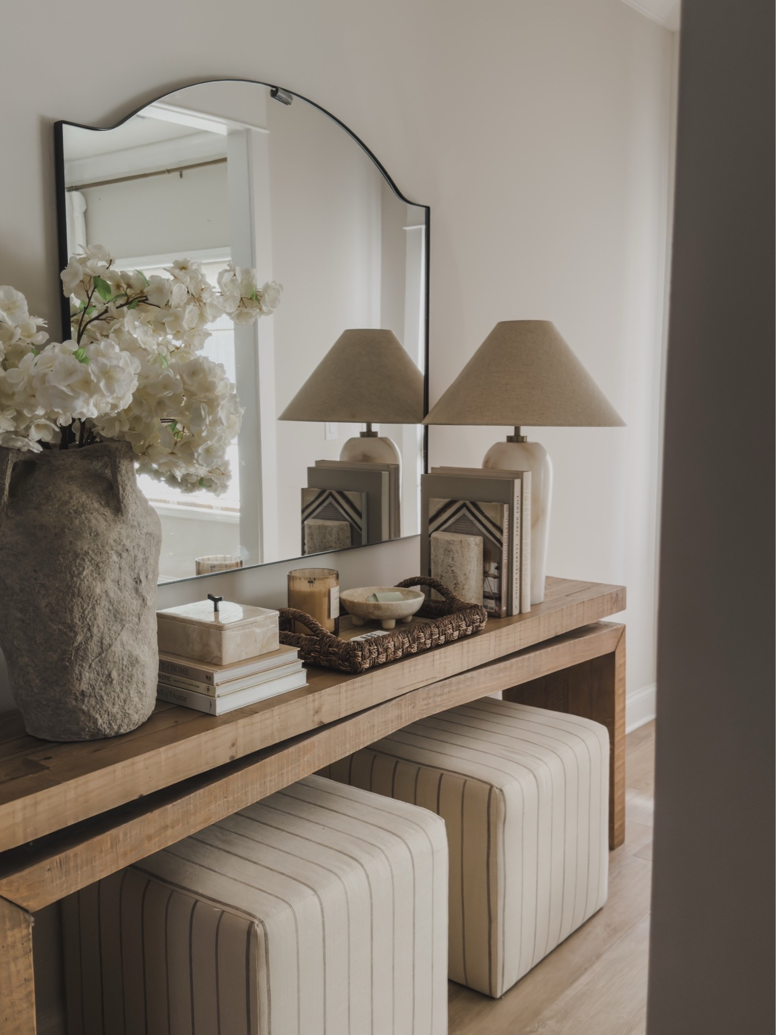 My front entryway is officially styled for summer.

This solid wood console table in Sierra Rustic Natural has been one of my favorite pieces I’ve brought into our home. The wood tone is beautiful, the quality is incredible, and it provides the perfect spot for seasonal styling. I paired it with these striped ottomans tucked underneath for extra seating when we have guests over.

For summer, I kept things simple with cherry blossoms, a few travertine accents, and my favorite woven HomeGoods tray that adds so much texture. The alabaster lamp gives off the prettiest glow in the evenings and is one of those pieces that makes the entire space feel warm and inviting.

I always find myself coming back to natural materials, subtle patterns, and pieces that are both beautiful and functional. This little corner checks all the boxes. 🤍

#LTKSeasonal #LTKSaleAlert #LTKHome