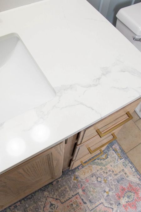 Engineered marble top on oak vanity with gold hardware. We love the boho rug we added to this space. #bathroomvanity #bathroomupdate #brassgoldfixtures #amazonhardware

#LTKhome #LTKfindsunder50