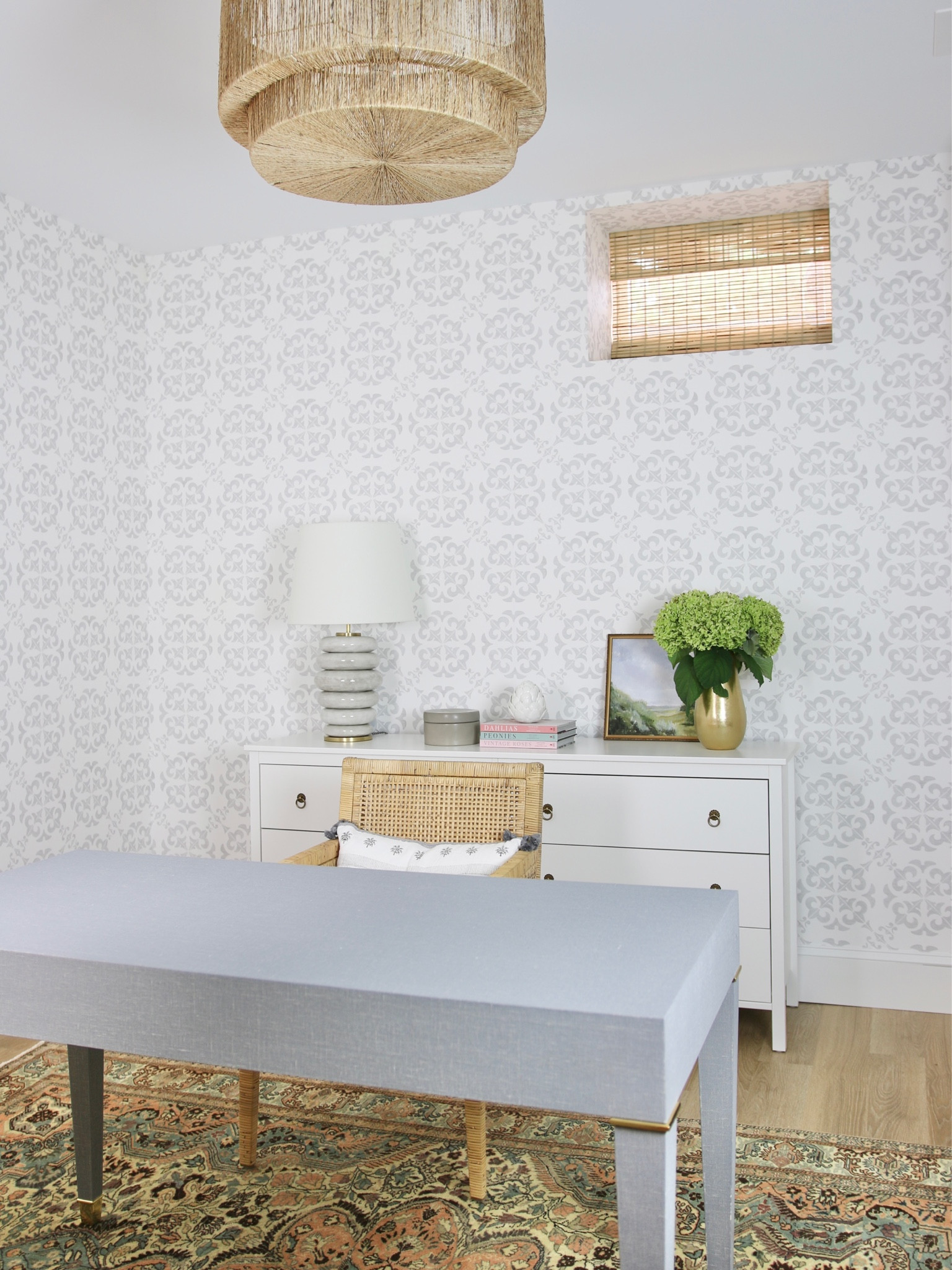 When I finished my basement I decided to use this room as an office. Ultimately I moved my work space upstairs but I was happy with how this turned out. 
I started with fog colored wallpaper and a bamboo Roman shade in the window. The overhead light is a woven pendant light.
I used a linen wrapped desk and rattan armchair as my workspace

#LTKhome #LTKFind #LTKstyletip