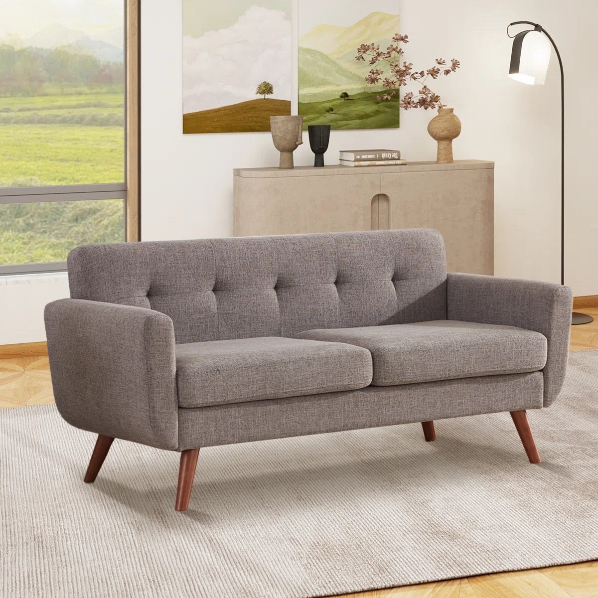 This gray upholstered loveseat from Wayfair is such a timeless piece for a living room or apartment. The square arms, tufted back cushions, and tapered wood legs give it a modern mid century feel that is both stylish and cozy. Perfect paired with a neutral area rug, console cabinet, and simple wall art.