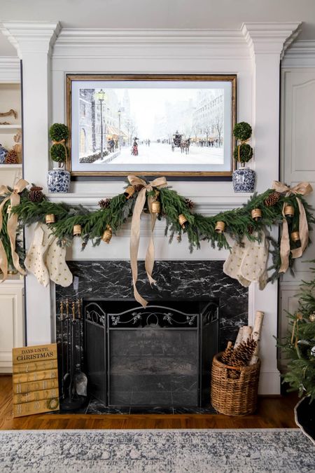 The blue and white living room is finished for Christmas decor! Mantel garland with bells, gold bows, blue and white ginger jars, boxwood topiaries, frame tv with Christmas frame tv art.

#LTKHoliday #LTKSeasonal #LTKhome