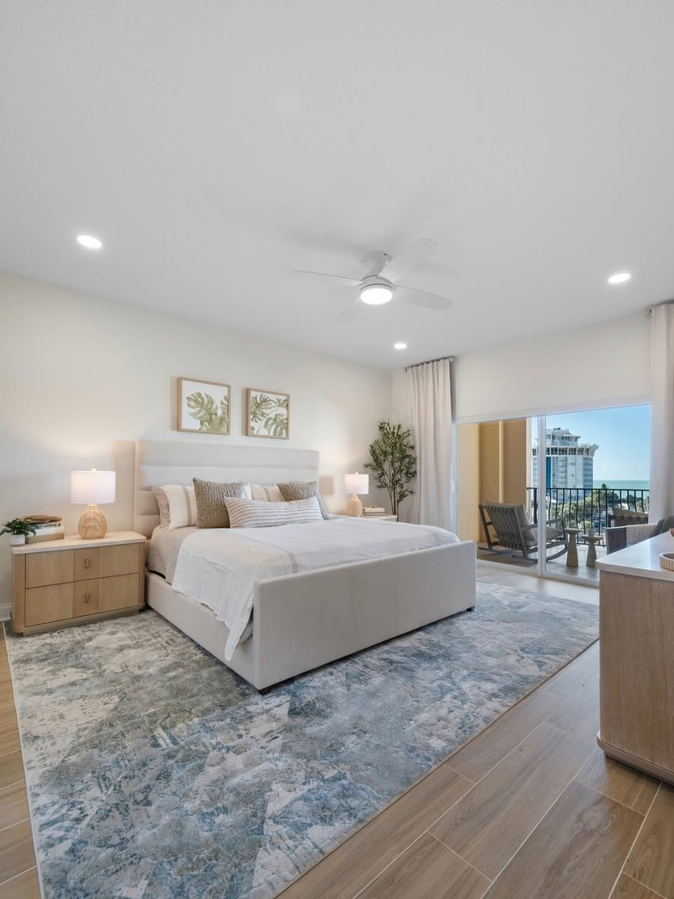 Close-up of a modern bedroom featuring a light-colored upholstered bed, textured area rug, and wood flooring that bring warmth and sophistication to the space. Two nightstands with elegant lamps and curated decor add layered detail, while glass sliding doors and soft recessed lighting create an airy, serene retreat. #TimelessBedroomDecor #LayeredBeddingInspo #LTKHome 

 