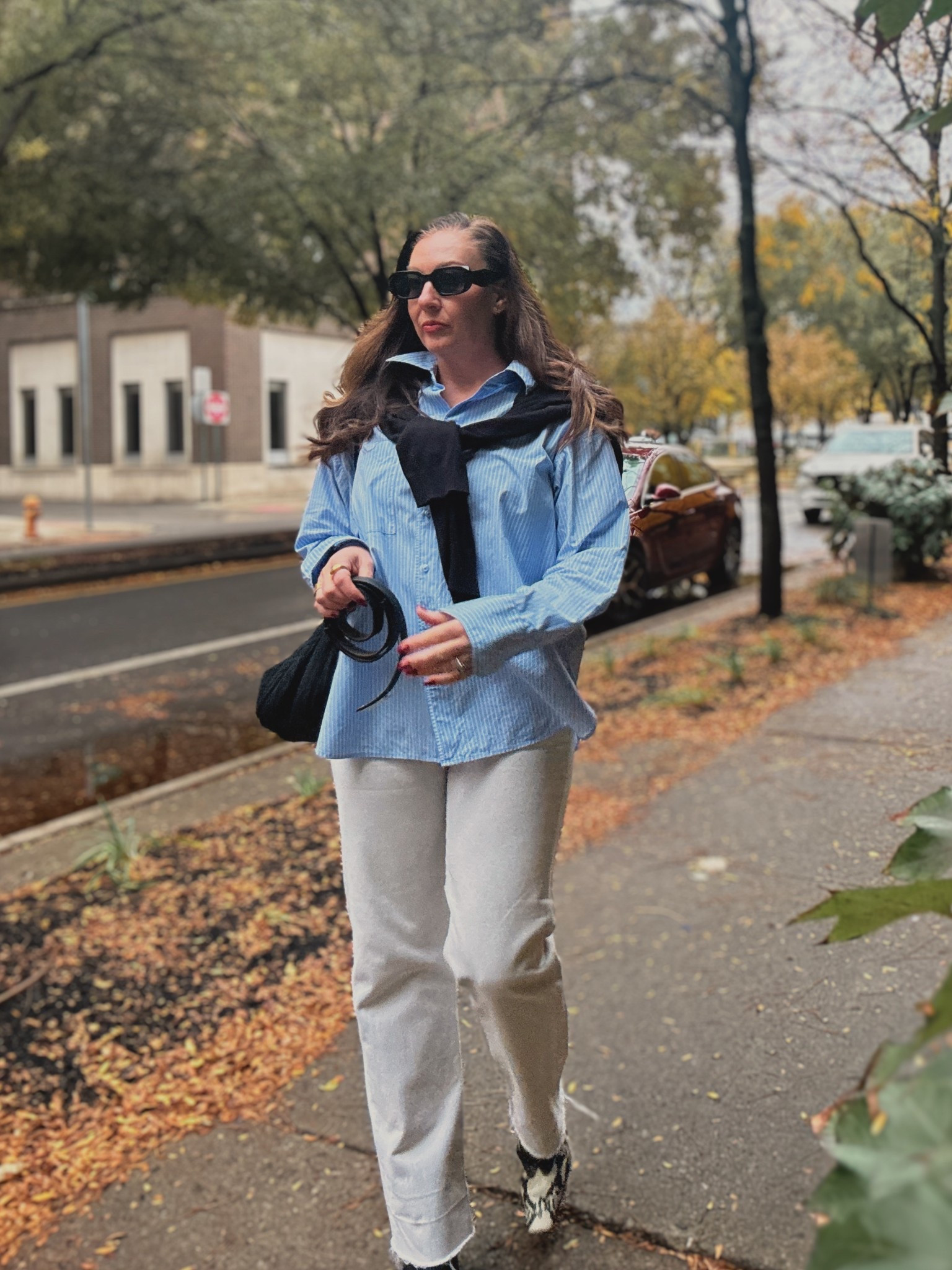 Fall style. Street style. Blue striped shirt. Light straight leg jeans. Khaite boots. Preppy style. Crossbody bag. Black sweater. 

#LTKStyleTip #LTKFindsUnder50 #LTKOver40