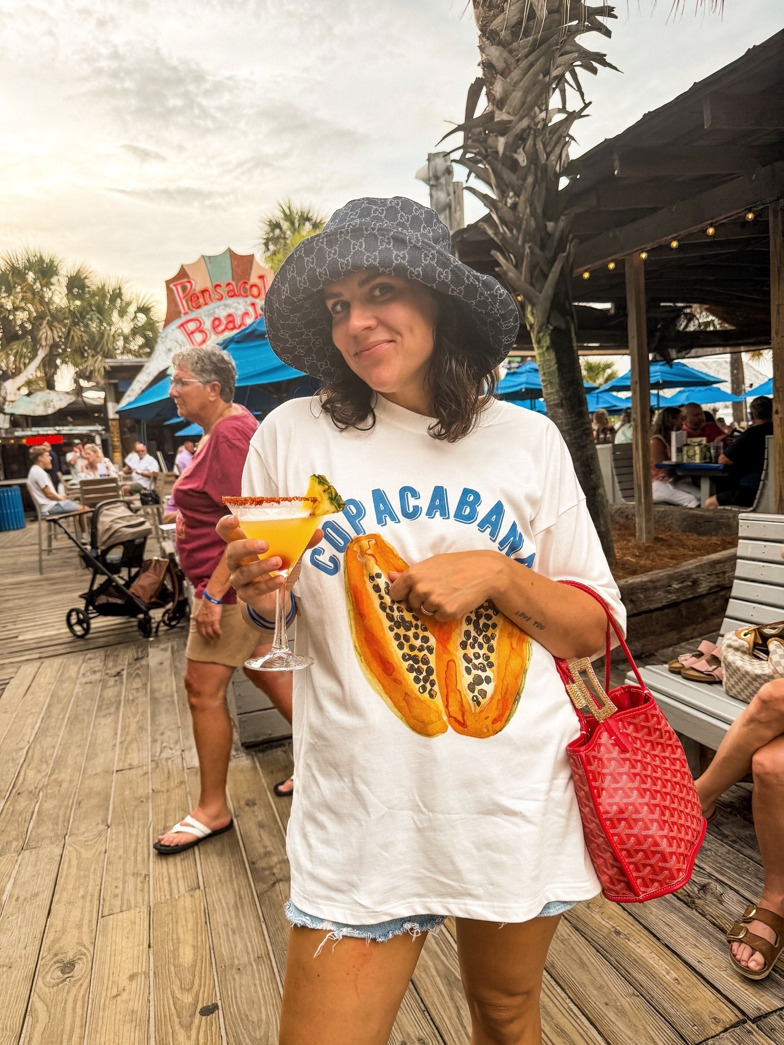 Beach bar outfit 🍹☀️ Oversized graphic tee, denim shorts, designer bucket hat & tropical cocktail vibes in Pensacola Beach 🌴 #LTKStyle #BeachOutfit #VacationStyle #SummerFashion #DesignerInspired #CasualChic #ResortWear #DenimShorts #BucketHatStyle #BeachVacation