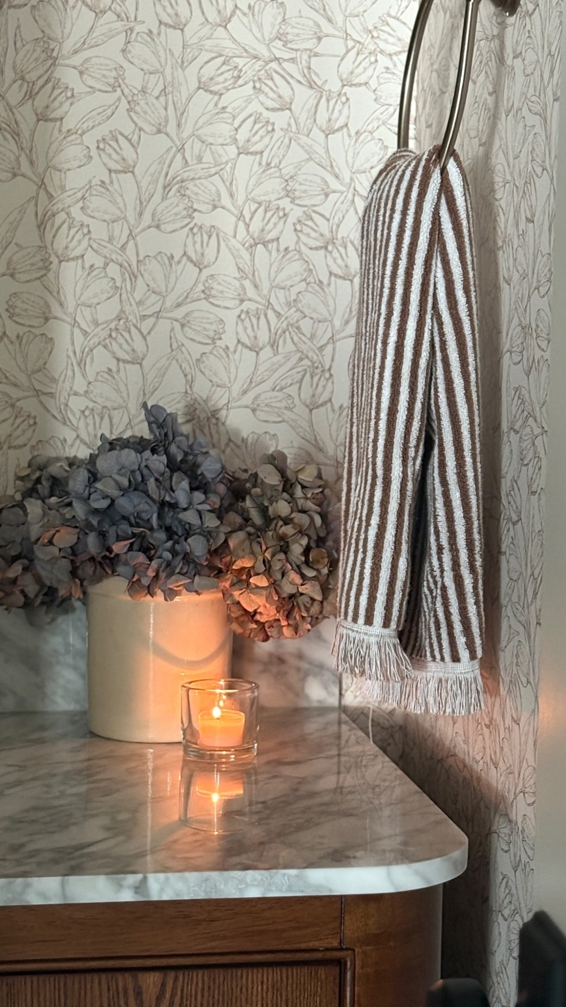 Cozy moments meet timeless style. 🤎 This small bath vignette feels instantly elevated with soft lighting, warm wood tones, and textured accents — from the striped terry towel to the hydrangeas that bring subtle color and life. Proof that even the smallest corners can feel intentional and inviting.

#HomeDecor #PowderRoomGoals #BathroomStyling #NeutralHome #OrganicModern #CozyHome #HydrangeaDecor #LTKHome #HouseOfSaint #MarbleCountertops #WarmNeutralDecor #FallHomeStyle 

 #LTKHome
