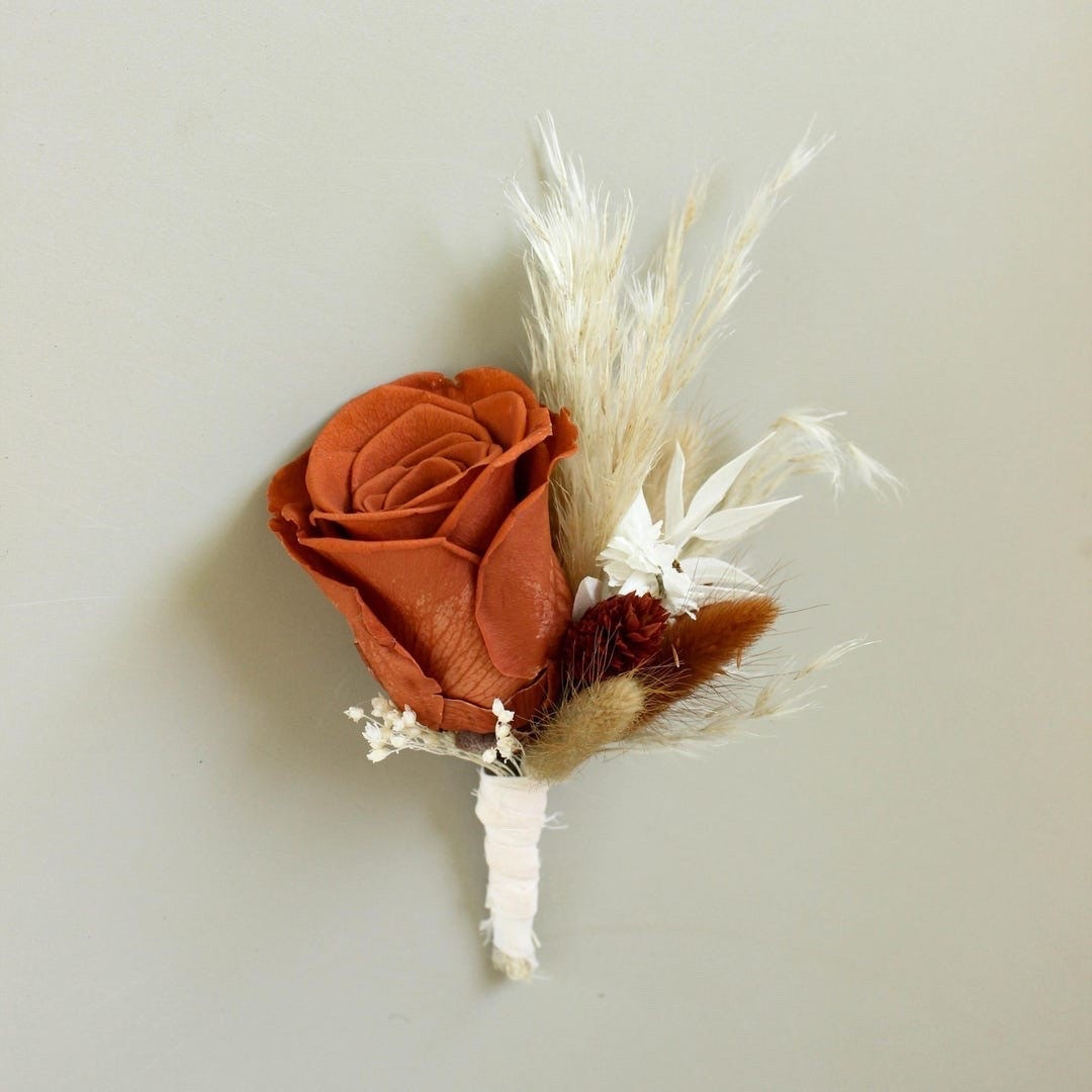 This handcrafted dried flower boutonniere features a rich rust rose accented with pampas grass, bunny tails, and white ruscus for a warm, romantic look. Perfect for grooms, groomsmen, and rustic weddings, this timeless accessory adds natural texture and lasting beauty to your special day. Finished with soft rayon ribbon and includes two pins for easy attachment. #DriedFlowerBoutonniere #RusticWedding #GroomStyle #BohoWedding #WeddingAccessories #PreservedFlowers #GroomsmenStyle #EverlastingFlowers #LTKWedding #WeddingDetails

#LTKWedding #LTKMens #LTKSeasonal