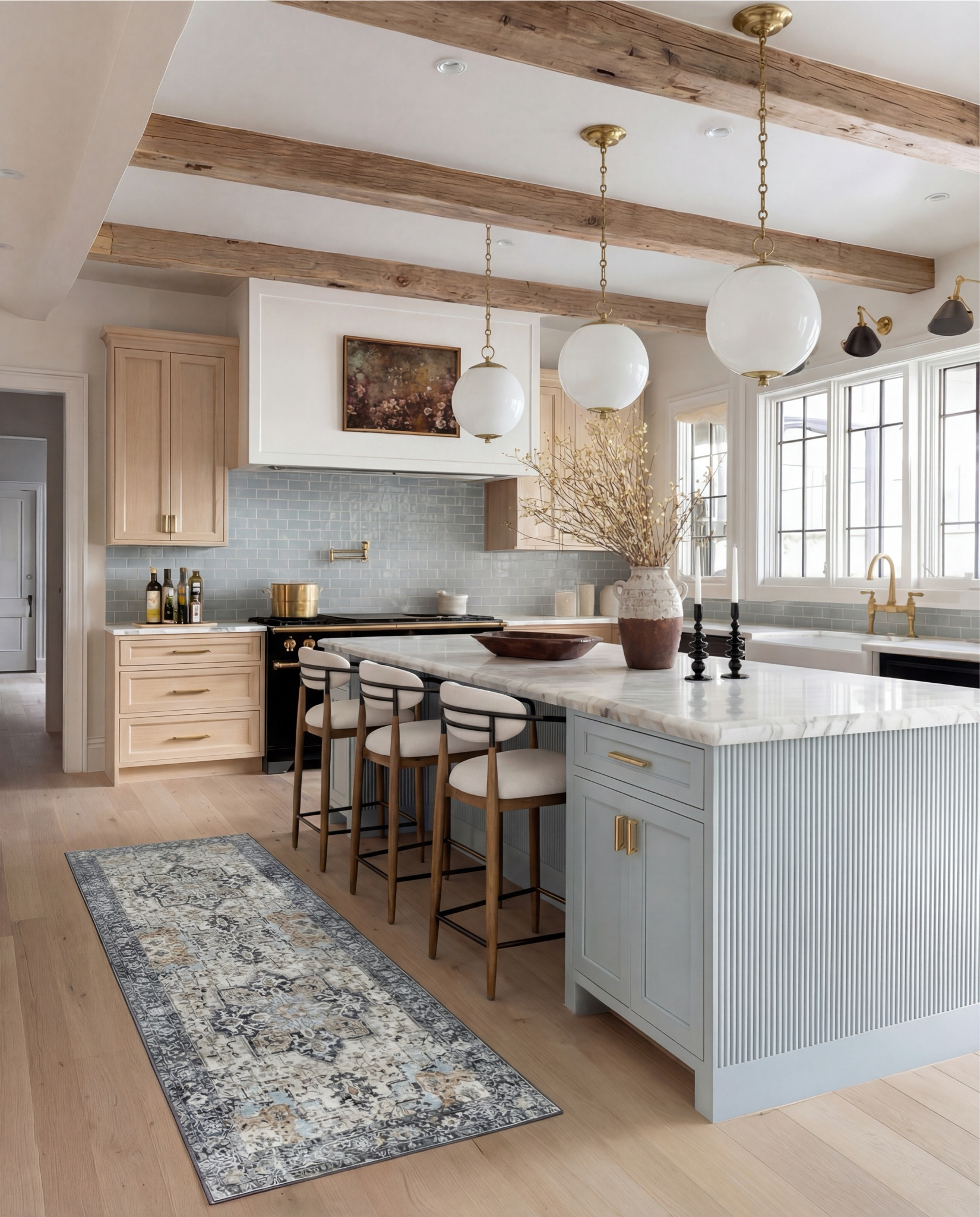 This kitchen is the definition of soft luxury done right. The pale blue island brings a calm, collected energy, while the warm oak cabinetry and exposed beams add that natural depth you can’t fake.

The oversized globe pendants keep everything feeling airy and modern, and the marble countertop? Effortless elegance. Even the runner pulls the whole palette together with those muted blues and warm neutrals.

It’s the kind of space that feels lived-in yet elevated—where morning coffee somehow tastes better and slow dinners feel intentional.

Shop the Look:
• Light blue fluted kitchen island
• Warm oak kitchen cabinets
• Brass globe pendant lights
• Marble kitchen countertop
• Neutral blue patterned runner
• Black + brass bar stools
• Soft blue subway tile backsplash
• Brown Ceramic vase with branches
• Gold kitchen faucet and hardware
•Brown bowl 
Brown floral wall art
Black candle holder

#LTKHome #LTKFindsUnder100 #LTKSaleAlert