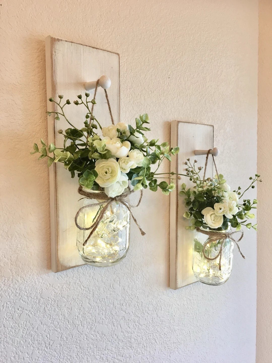 Add a personalized farmhouse touch to your walls with these handcrafted mason jar sconces by CountryHomeandHeart. Made from premium pine wood and finished with charming jute accents, each piece includes your choice of florals for a look that fits your style perfectly. With the option to add soft LED fairy lights, these sconces create a warm, cozy glow—making them perfect for bedrooms, hallways, or any space that could use a little extra charm. #LTKHome #FarmhouseDecor #MasonJarDecor #WallSconces #CozyLighting #RusticStyle #HomeStyling #PersonalizedDecor

#LTKHome #LTKSeasonal #LTKWedding