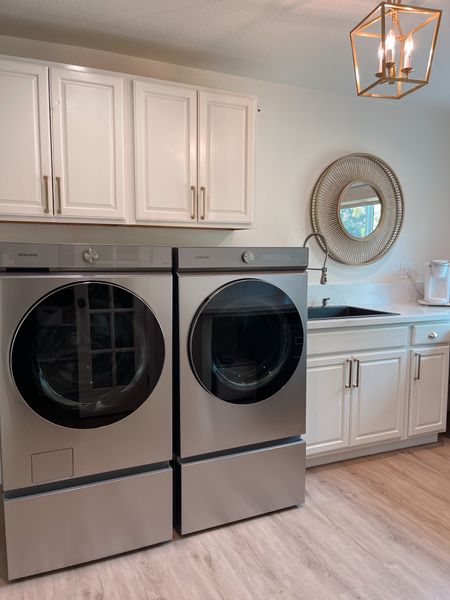 Simple elegant clean modern white and gold laundry room. Pearly White by Sherwin Williams painted cabinets. Alabaster on the walls. Champagne bronze cabinet pulls and gold handles. Raised wash machine and dryer. Laundry pedestal. Rattan round mirror. Gold pendant light fixture. 

#LTKhome #LTKFind #LTKsalealert
