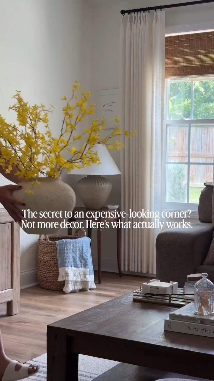 Corner decor can be difficult! Here are 5 ways that can help create an intentional space for any space! 👇🏼

1. Height that feels intentional, not crowded: floor to ceiling curtains and artwork pull the eye up and give the corner structure without needing more pieces. 

2. Grounding the corner by adding baskets: this anchors the space and adds warmth at floor level so the corner table doesn’t feel like it’s just “floating” in space

3. Negative space makes it feel expensive, but that’s just my opinion. Less is more for me 🤌🏼. Nothing is overfilled. The empty wall and breathing room are what create that calm, elevated feel.

4. Repetition of natural texture is 🔑: the woven basket + organic stems + mixing wood tones creates a curated space.

5. Colors! I’m a warm neutral girly, but here’s how contrast works together: the blue and yellow don’t “match,” but they complement the organic tones. It’s gentle. Versus doing colors like blue and pink would compete and fight for attention. Greenery is a safe option!

See anything you like? Comment SHOP to copy the look! 🔗 

#stylewithme #cornerstyling #homestylinghacks #neutralhomestyle #livingroomideas