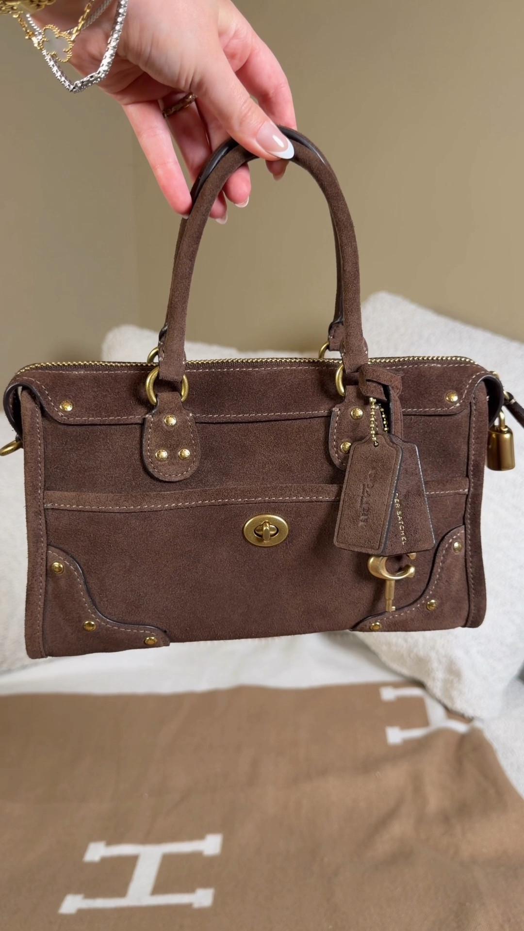 Shes currently out of stock but I linked it so you can check for restocks & I linked some similar-ish bags🤎 Comment SHOP & I’ll dm you the link 🤎

This is the Coach Rhyder satchel 24 re-edition in chocolate suede. I love how boxy yet squishy the design is and all of the hardware buttons. The suede, patches and brass buttons give me major western vibes which I love for summer and fall 😍