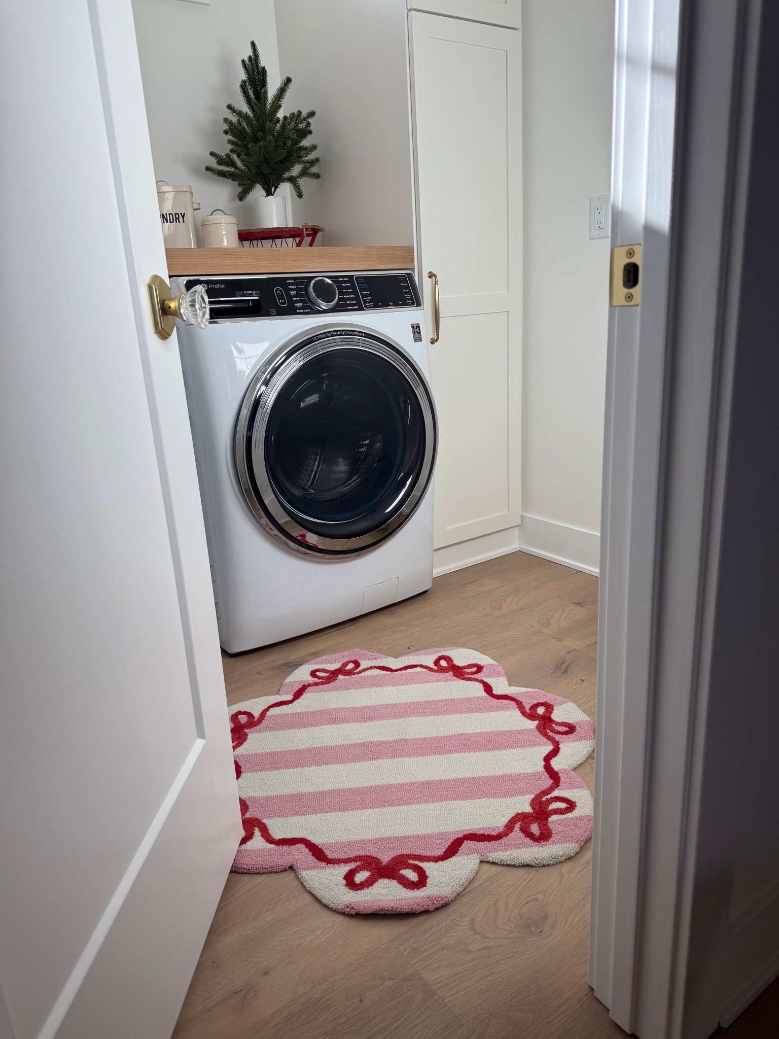 Pink stripe and red bow rug with scallop detail! Faux tree in scalloped pot! 
New build home finishes in honey bronze! Crystal door knob! 

#LTKSeasonal #LTKHoliday