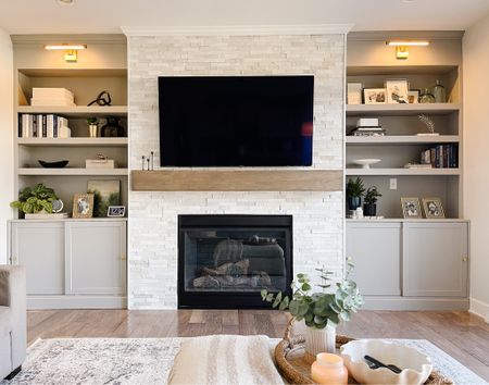 Living room fireplace with built in cabinets on both sides
Marble stacked stone, wooden beam mantle, built in shelves, picture lights, living room storage 

#LTKstyletip #LTKFind #LTKhome