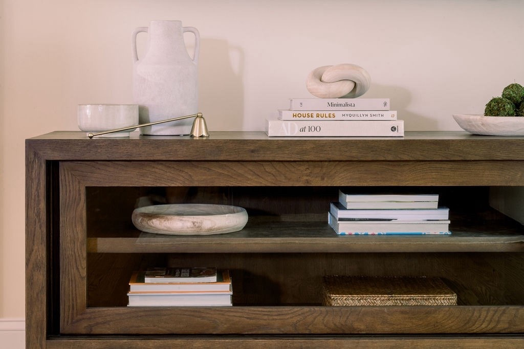 Neutral, clean & timeless styling ✨
This wood TV stand is the perfect mix of function + style. I kept the decor minimal: stacked design books, a sculptural knot accent, ceramic vase, and a  catch-all bowl. The glass shelving makes it feel light while still giving storage for books + baskets. A chic setup that works in any living room 🤍