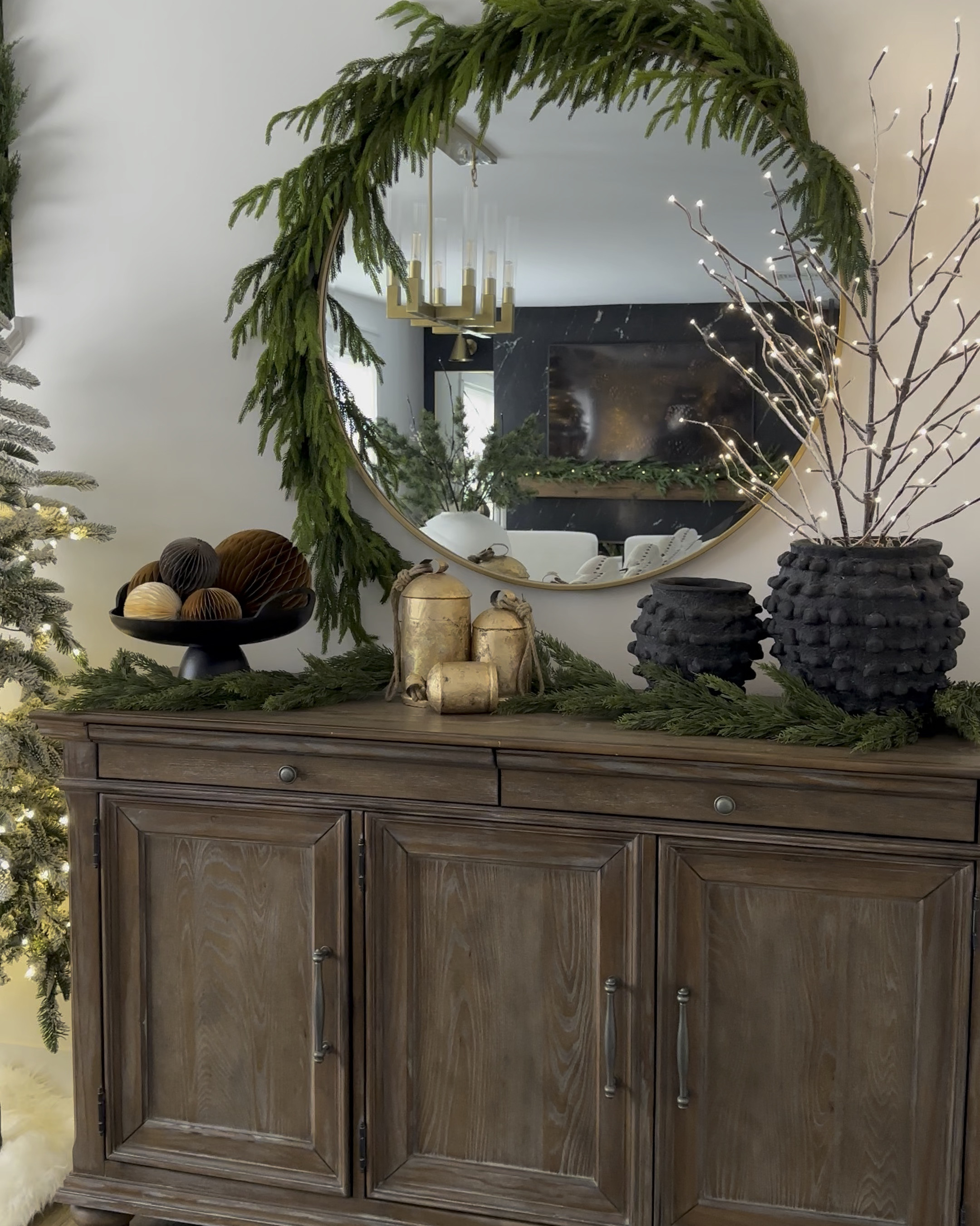 Holiday console table styling. Dining room side board. Christmas decor. Modern organic, neutral style. Norfolk pine garland, black vase, twinkle trees, mini Christmas trees, gold holiday bells, accordion ornaments, round mirror  

#LTKHome #LTKHoliday