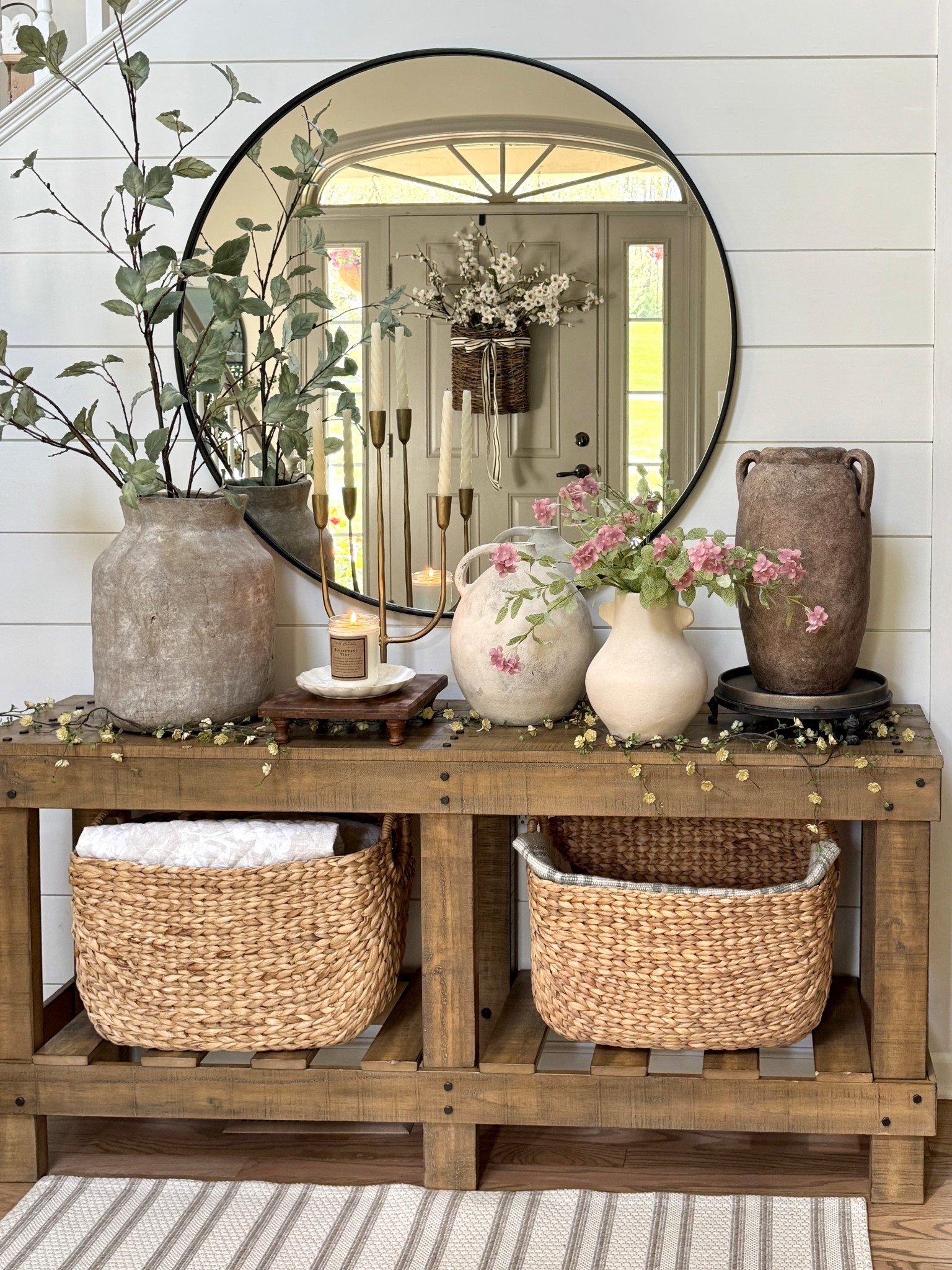 Entryway table styling:

Very large vase (on left side of table)
Faux sage stems - tall and make such a statement. 
Round wall mirror
Solid wood entryway table 
Tall baskets
Door basket and florals 
Pedestal risers
Candelabra 
Patterned square wood riser
Scalloped plate



#LTKHome