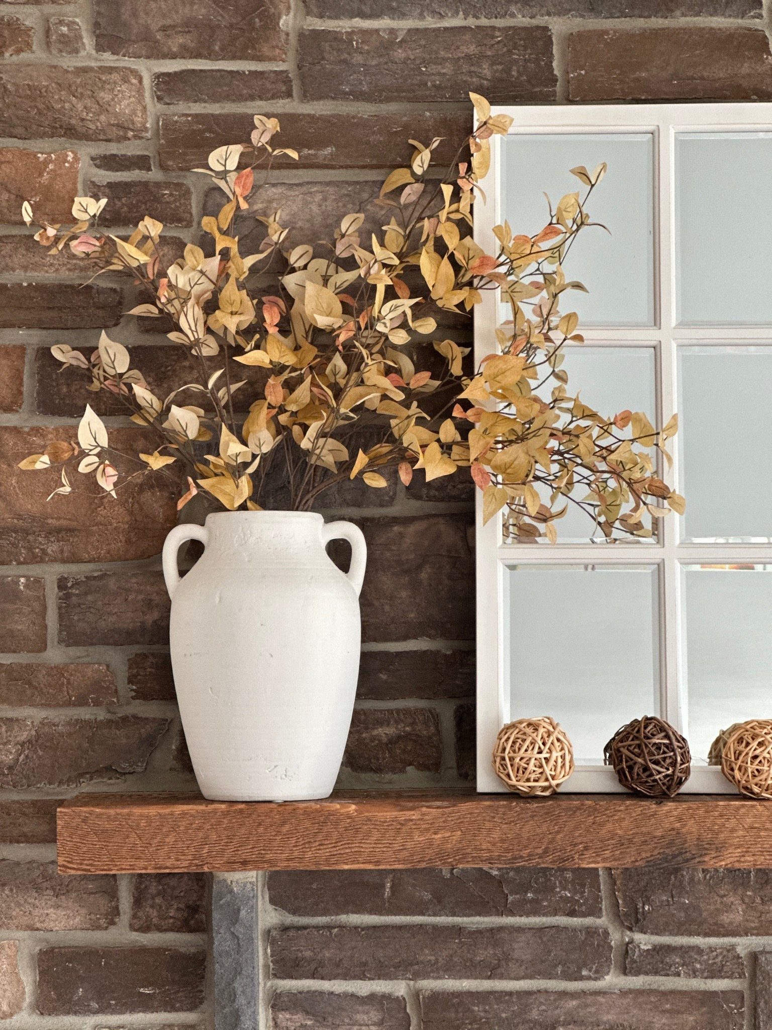Fall decor for the fireplace mantel.  Simple faux fall foliage stems in a white vase makes an impact next to a white window pane mirror and woven orbs.

#LTKSeasonal #LTKHome
