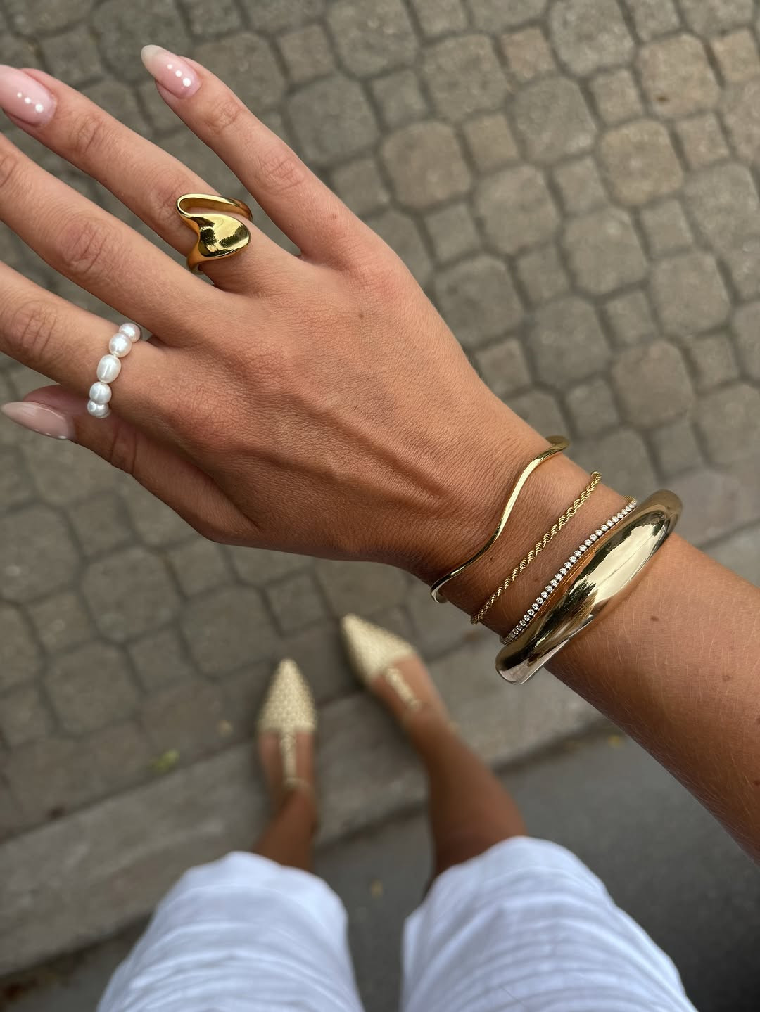 Golden stack. This accessory-focused look features a curated mix of gold bangles, a sculptural statement ring, and a delicate pearl band, paired with metallic woven flats. #GoldJewelry #RingStack #LTKaccessories 

 #LTKdayinmylife #LTKgrwm #LTKootd