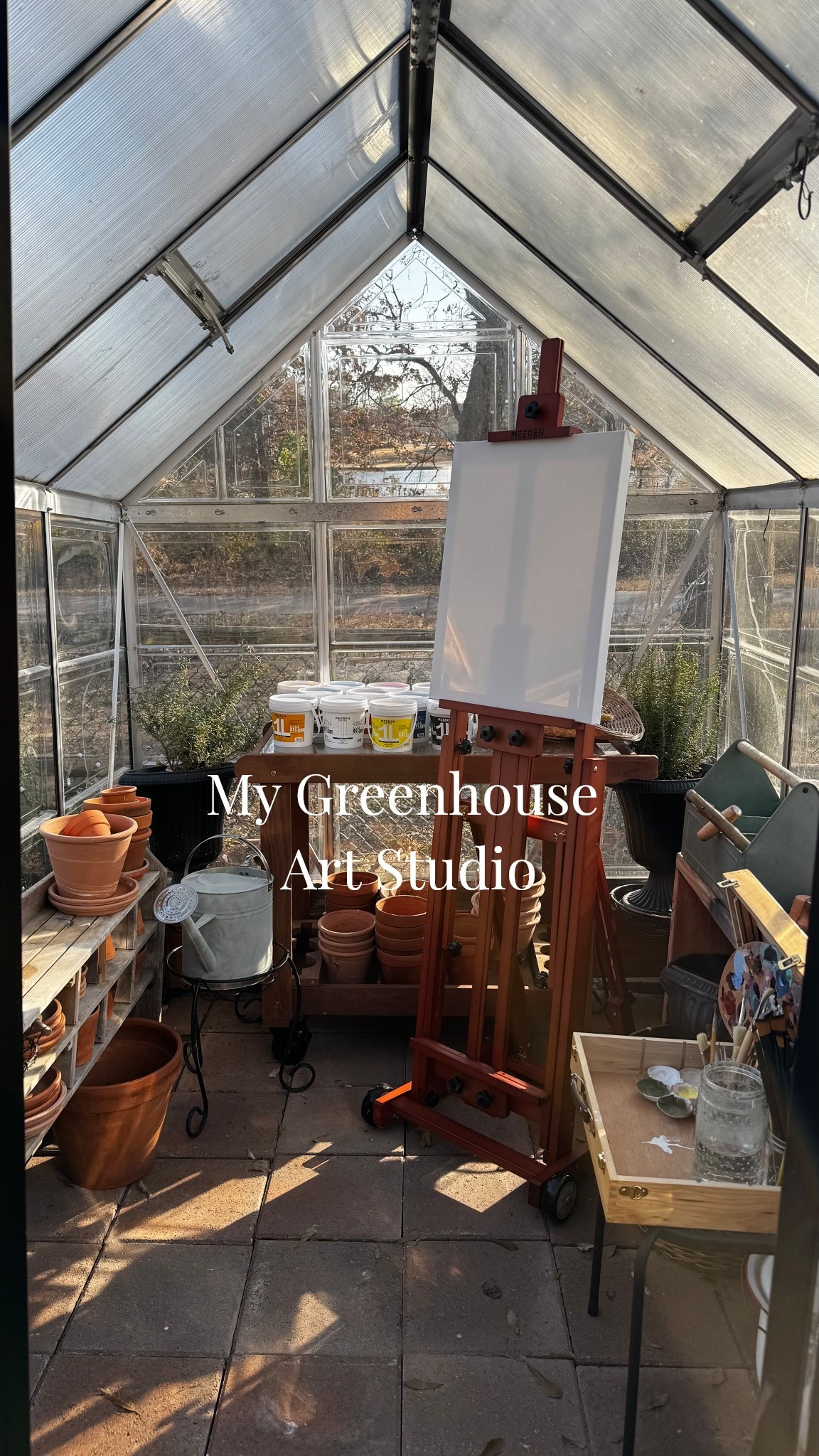 Transform your backyard greenhouse into the ultimate sun-drenched art studio. There is nothing more inspiring than painting surrounded by plants and natural golden hour light. The perfect cozy nook for artists and gardeners alike. #artstudio #greenhouselife #creativespace #slowliving 