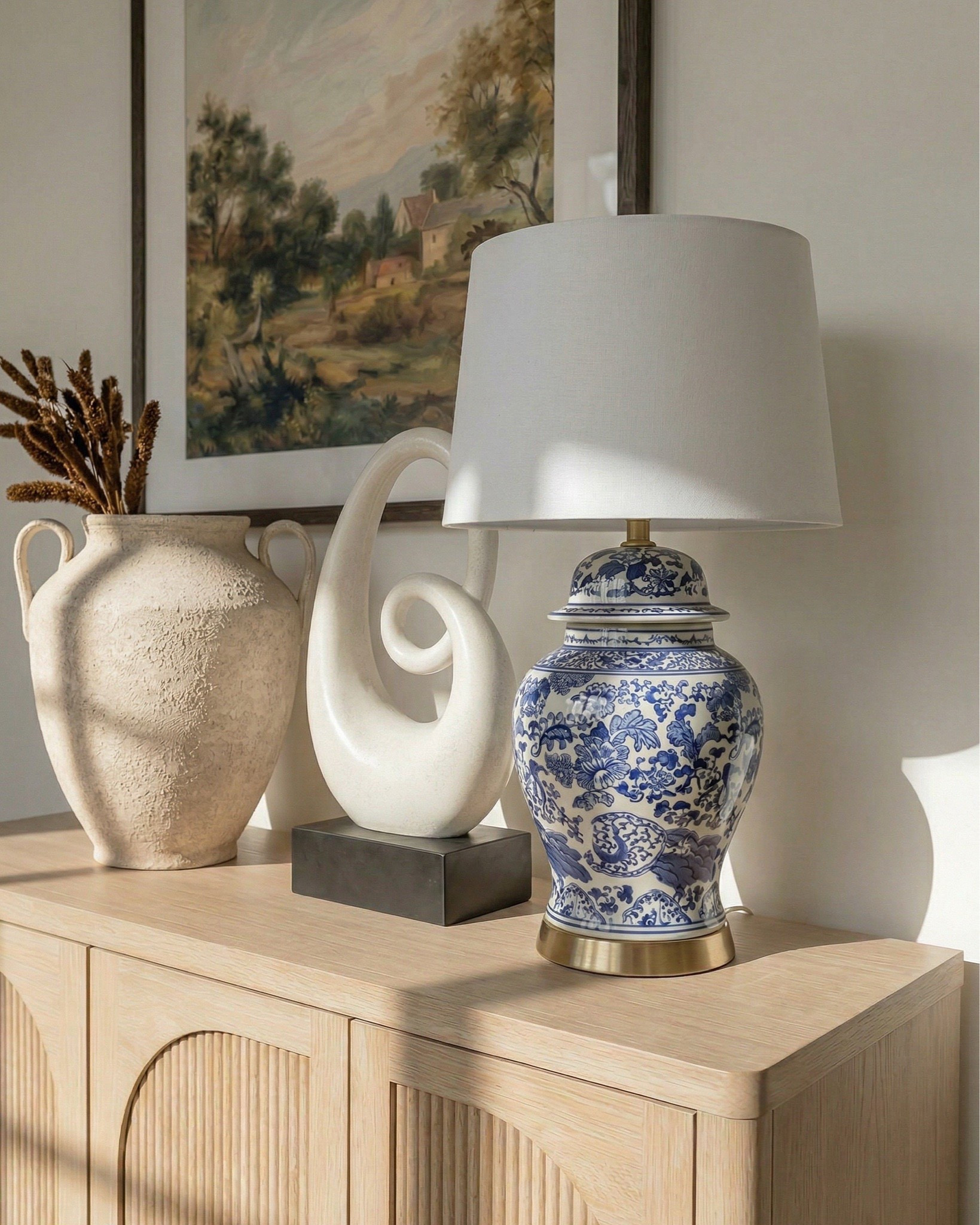 * Rectangular light wood dining table (traditional trestle base)
* Woven cane dining chairs (natural oak frame)
* Neutral vintage-style area rug (distressed pattern)
* Brass modern chandelier (linear / sculptural arms)
* Rustic exposed wood ceiling beams (reclaimed look)
* Large black-framed sliding glass doors (industrial style)
* Dark ceramic vase (handmade / organic texture)
* Dried floral arrangement (neutral stems)
* Sculptural brass decorative bowl
* Black ceramic candle holder (modern abstract form)
* White taper candle
* Small matte black decorative bowl
* Minimalist sculptural object (black accent piece)
* Light wood sideboard cabinet (fluted / ribbed detailing)
* Built-in arched niche cabinet (custom millwork look)
* Decorative pottery (neutral ceramic vases)
* Framed landscape wall art (classic / muted tones)
* Indoor olive tree (or faux olive tree)
* Neutral linen / textured textiles
* Warm light oak flooring
* Soft cream / off-white wall paint
* Arched doorway architectural detail

#LTKHome #LTKSaleAlert