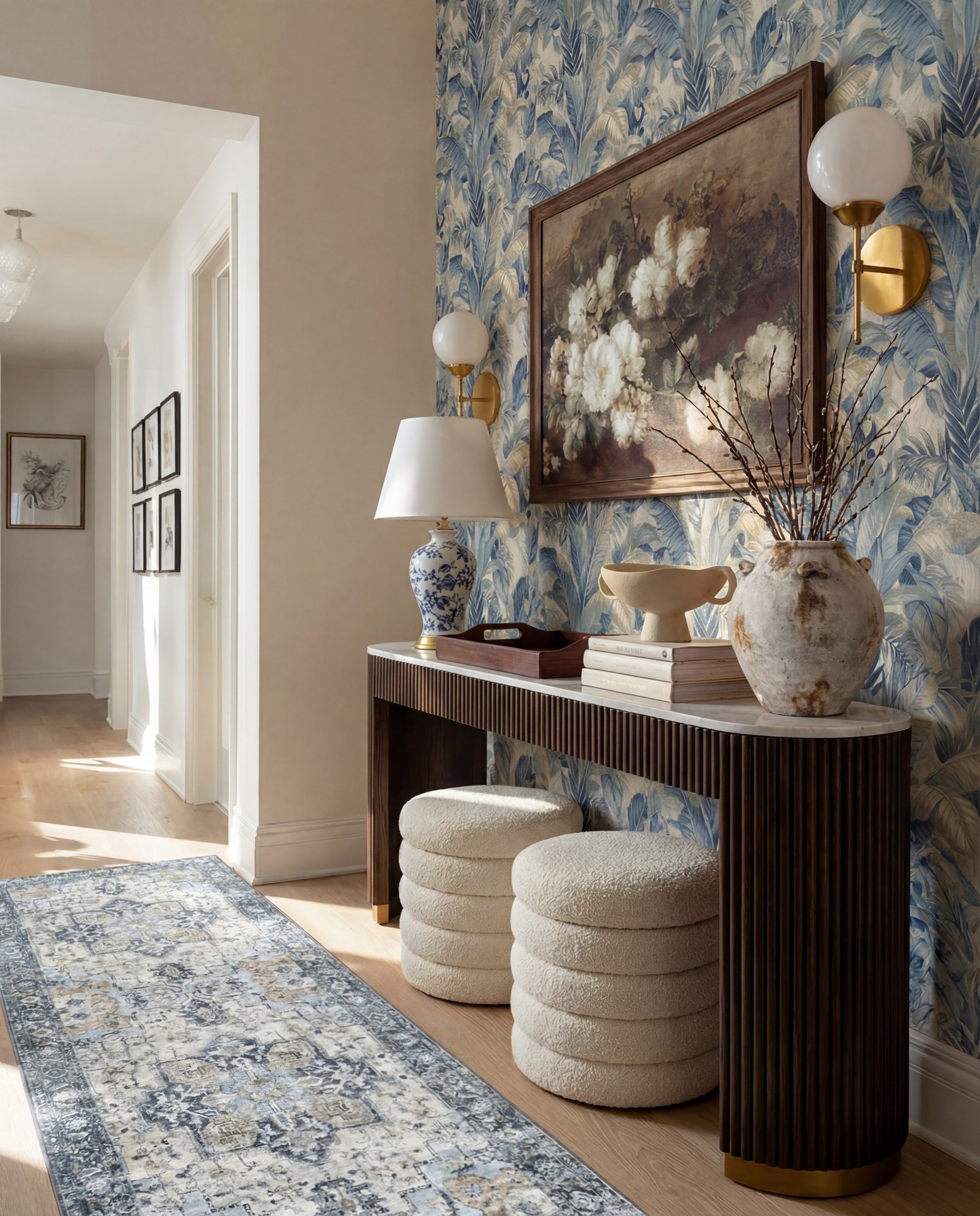 Shop the Look:
• Blue botanical wallpaper (leaf motif, muted navy + beige)
• Solid wood console table (dark walnut finish)
• Fluted wood console table legs
• White marble console tabletop
• Framed vintage floral wall art (dark wood frame)
• Brass wall sconces with white globe shades
• Blue and white ceramic table lamp
• White fabric lamp shade (tapered)
• Wooden decorative tray (rectangular)
• Stacked neutral coffee table books
• Sculptural ceramic bowl (cream stoneware)
• Distressed ceramic vase (antique white)
• Dried branches or twigs arrangement
• Bouclé ottomans (ivory, round)
• Light wood flooring
• White baseboards and trim

#LTKFindsUnder100 #LTKSaleAlert #LTKHome